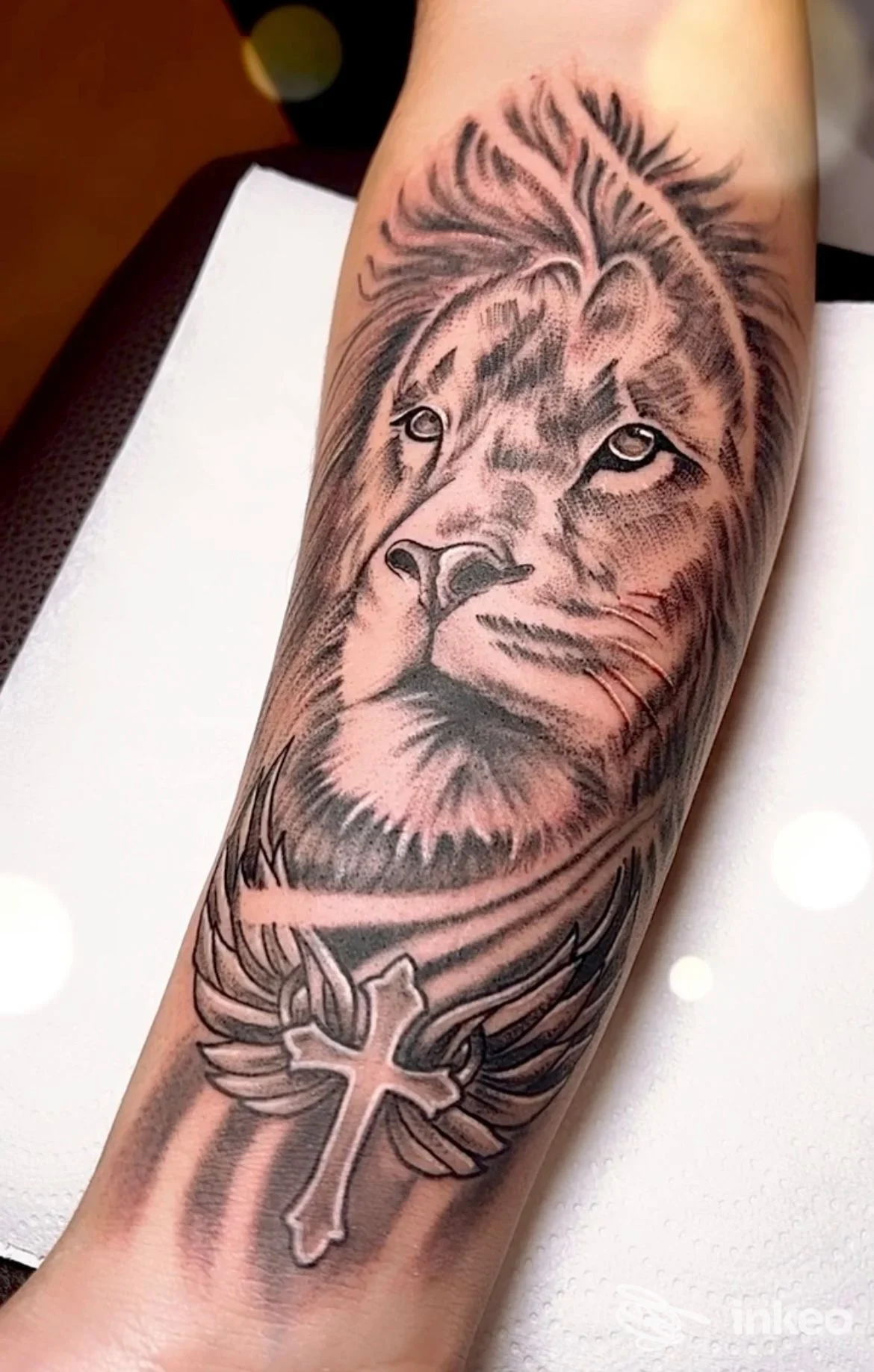 Tatuaggio sull'avambraccio con leone realistico e croce al polso, lavoro fotografato da ROBITATTOO STUDIO a Urbania.