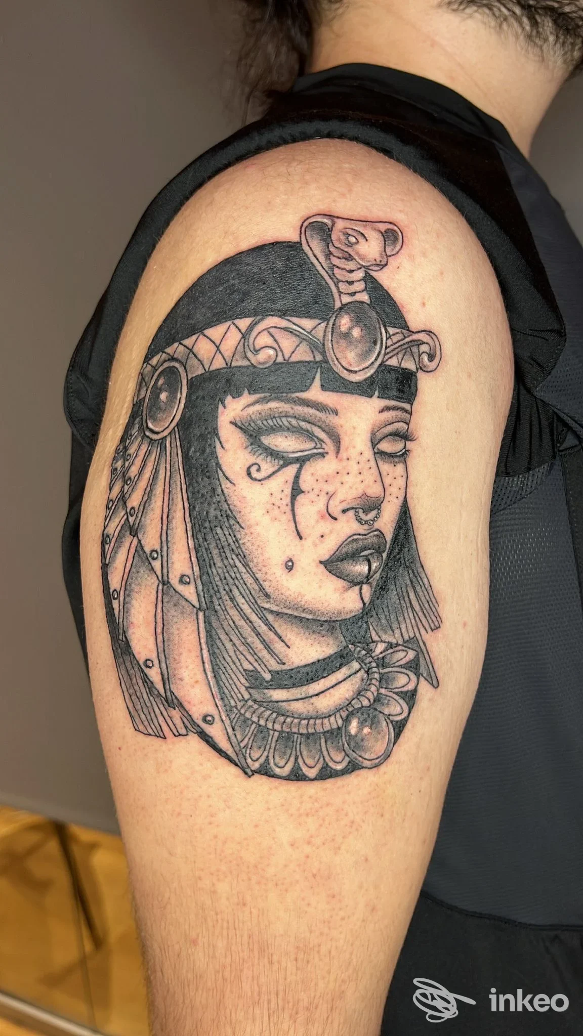 Tatuaggio black-and-grey su braccio superiore di volto egizio stilizzato, foto fornita da ROBITATTOO STUDIO, Urbania.