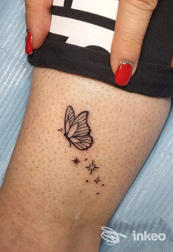 Piccolo tatuaggio nero di farfalla con stelline sulla parte superiore della gamba, foto da ROBITATTOO STUDIO, Urbania.