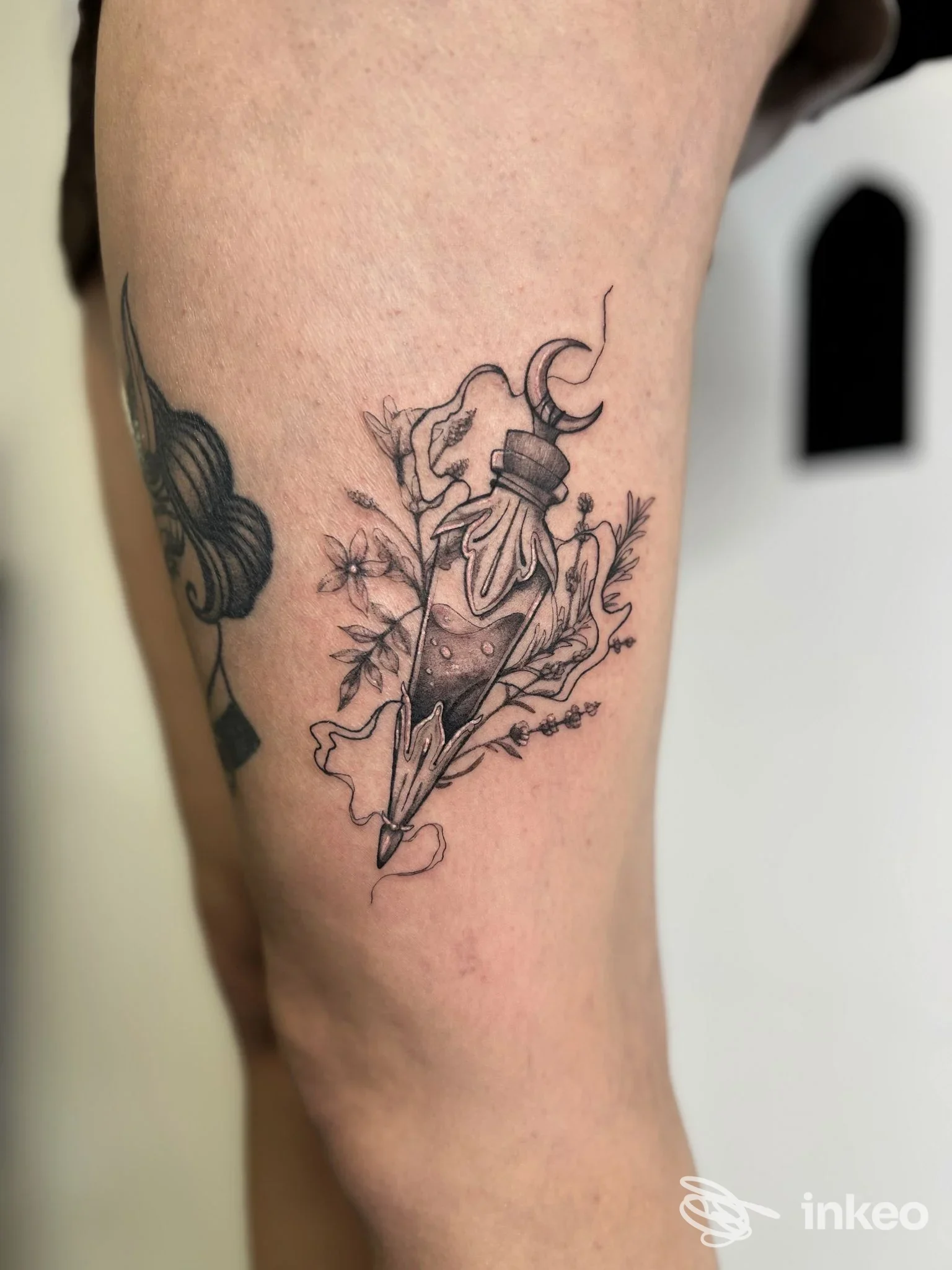 Tatuaggio su coscia con boccetta stilizzata e fiori, realizzato da SIBILLA TATTOO ROOMS, Sforzacosta.