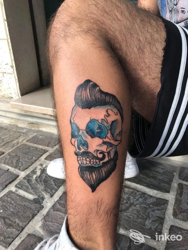 Tatuaggio su polpaccio con teschio e barba in nero e blu, foto inviata da Santeria Tattoo Studio a Chiaravalle.
