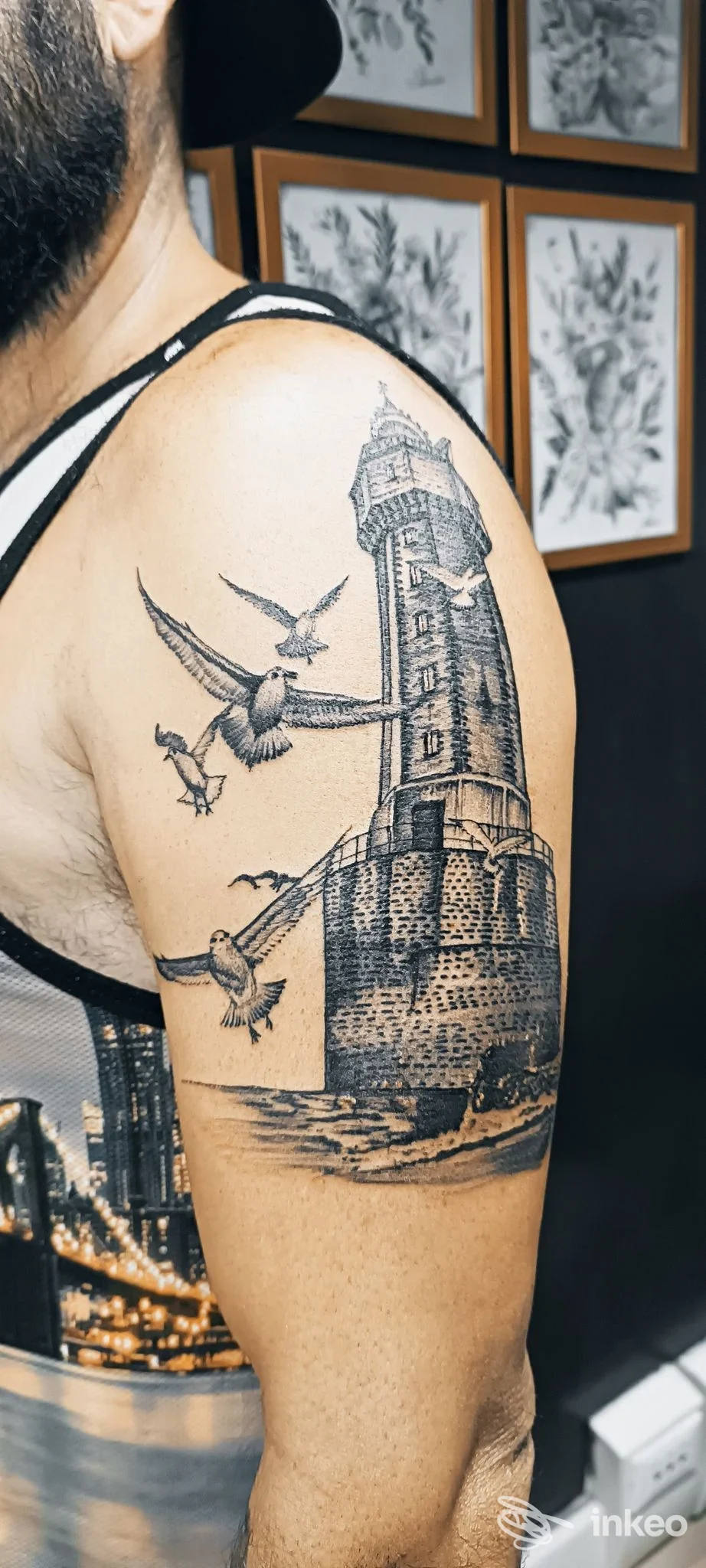 Tatuaggio realistico in nero di un faro con gabbiani sul braccio superiore, foto fornita da SalvitattooArtist a Marzocca.
