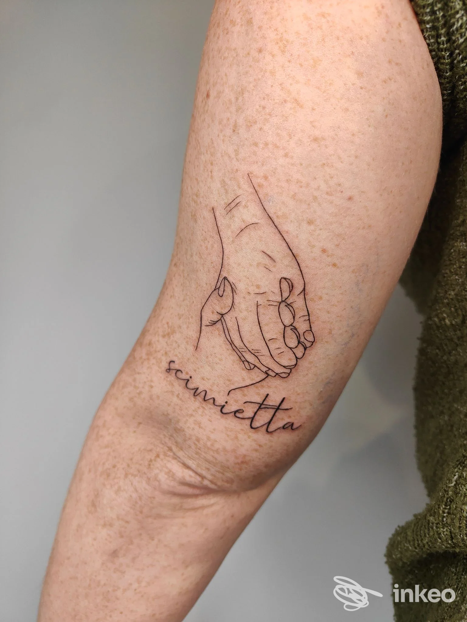Tatuaggio lineare di due mani che si tengono con scritta corsiva sul braccio, foto fornita da Sinsink tattoo studio a Monte Urano.