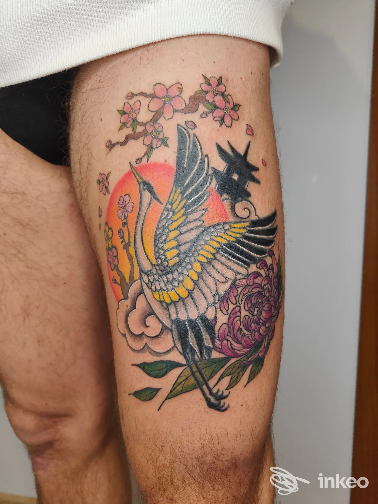 Tatuaggio su coscia con gru in volo, fiori e sole stilizzato, colori pieni e contorni netti — Sinsink Tattoo Studio, Monte Urano.