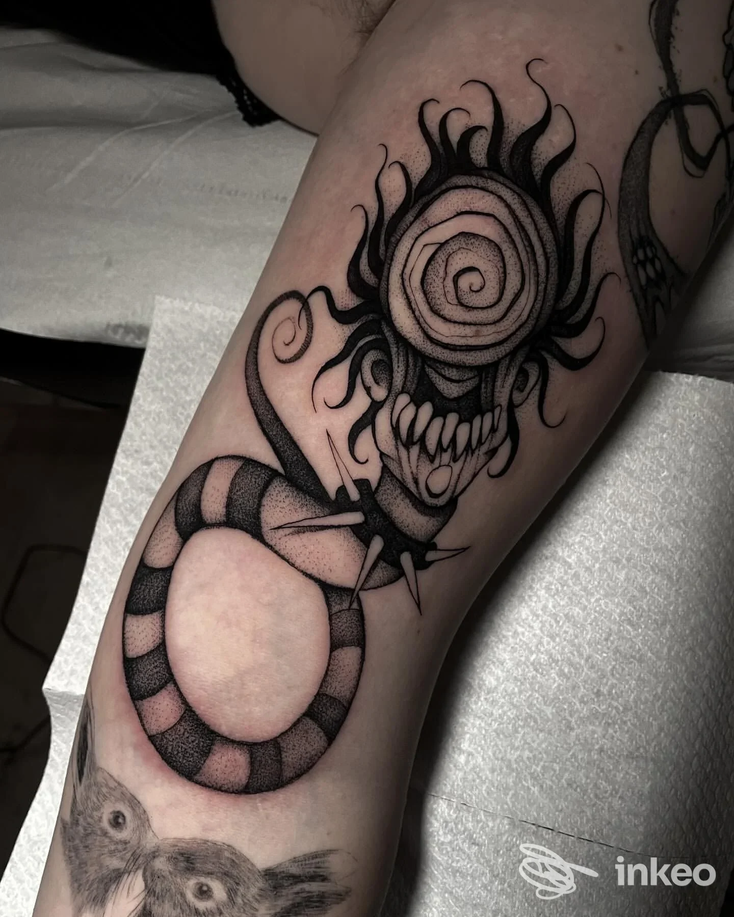 Tatuaggio su avambraccio con figura mostruosa a spirale e anello a strisce, Snatch Tattoo & Piercing, Osimo.