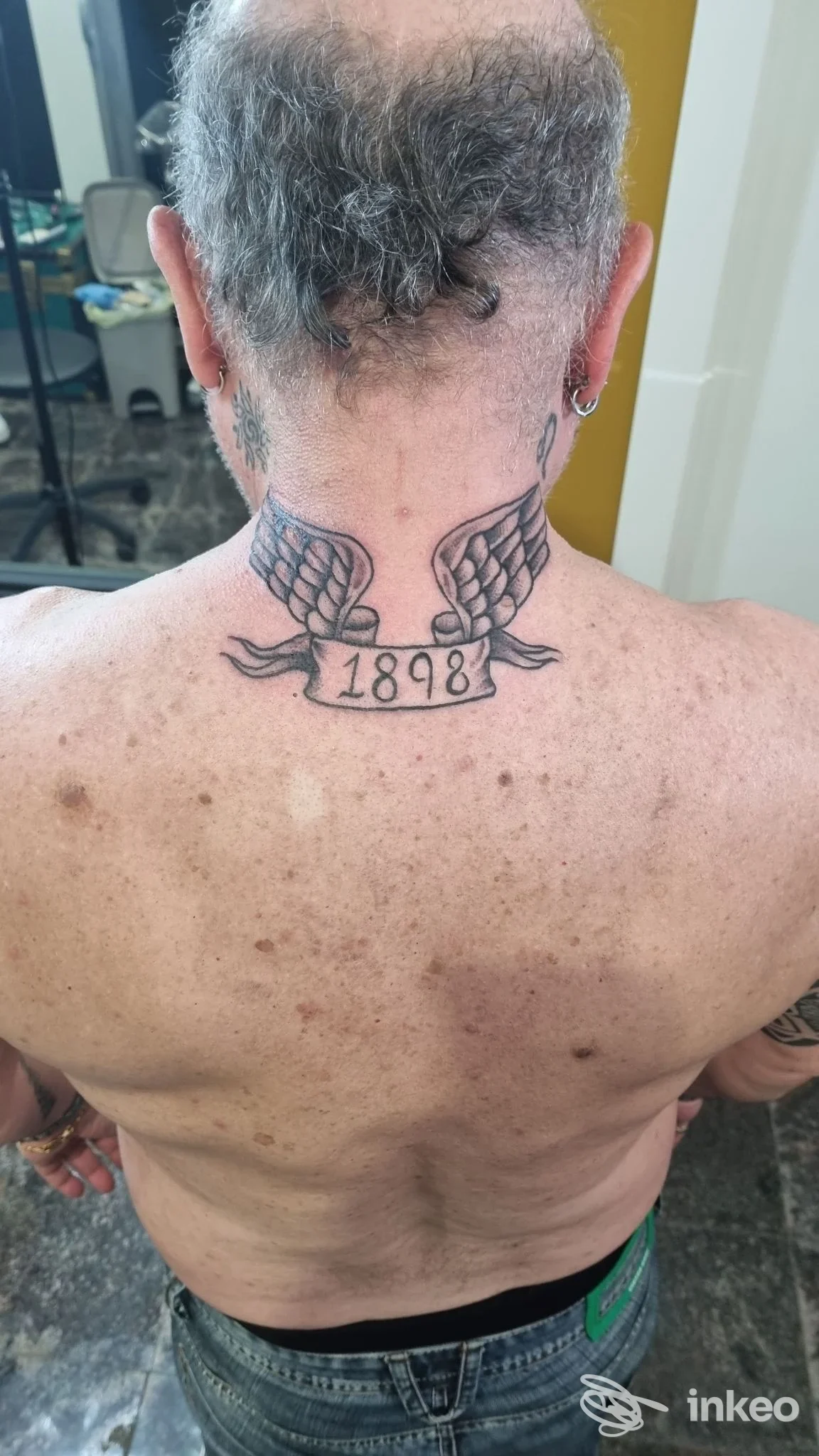 Fotografia del tatuaggio sulla nuca con ali e la data 1898, Stanza 103 Tattoo Studio, Villa Pigna.