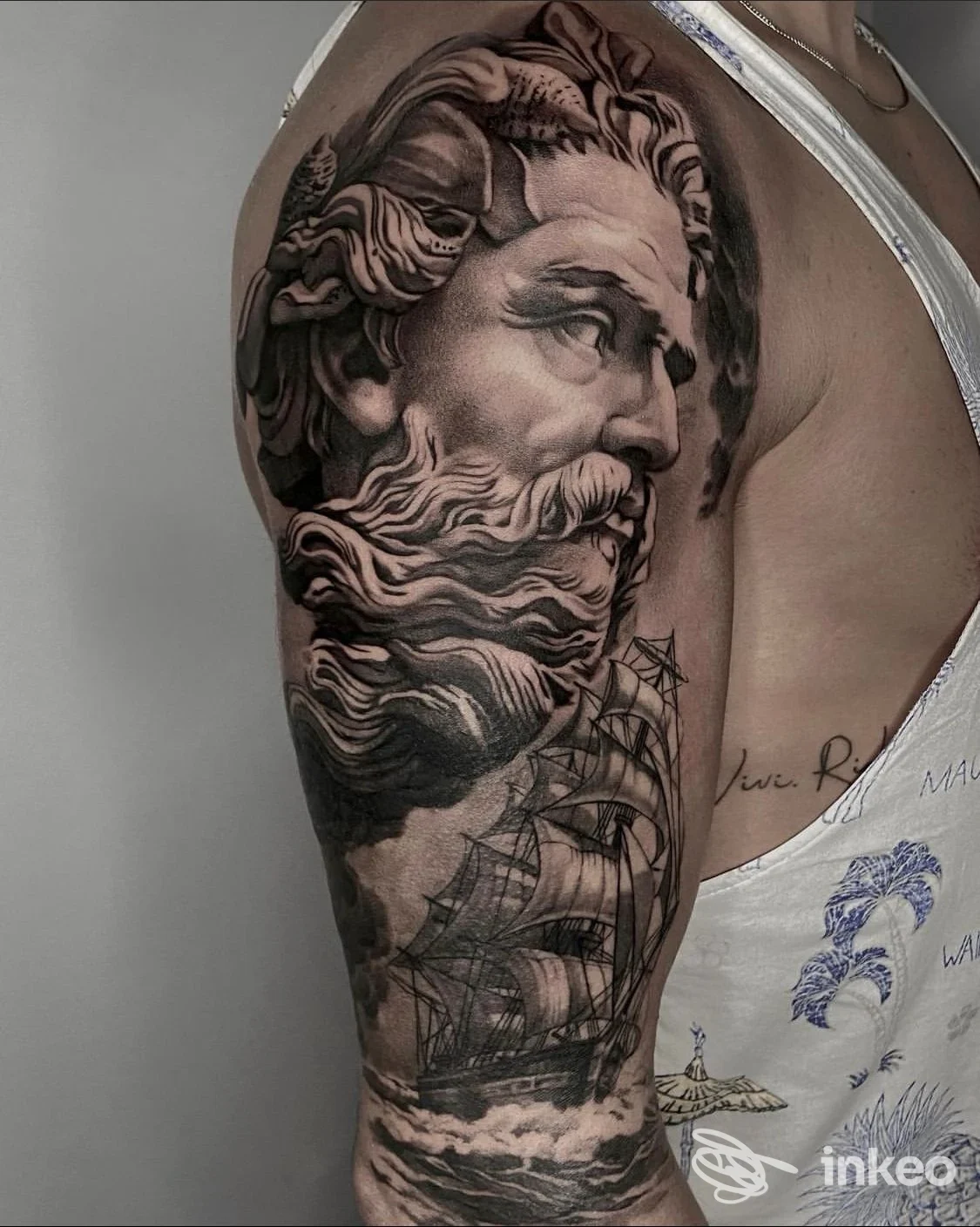 Tatuaggio a manica sull'alto braccio con volto classico e nave a vele, immagine fornita da Stlkr Art & Tattoo, Fossombrone.