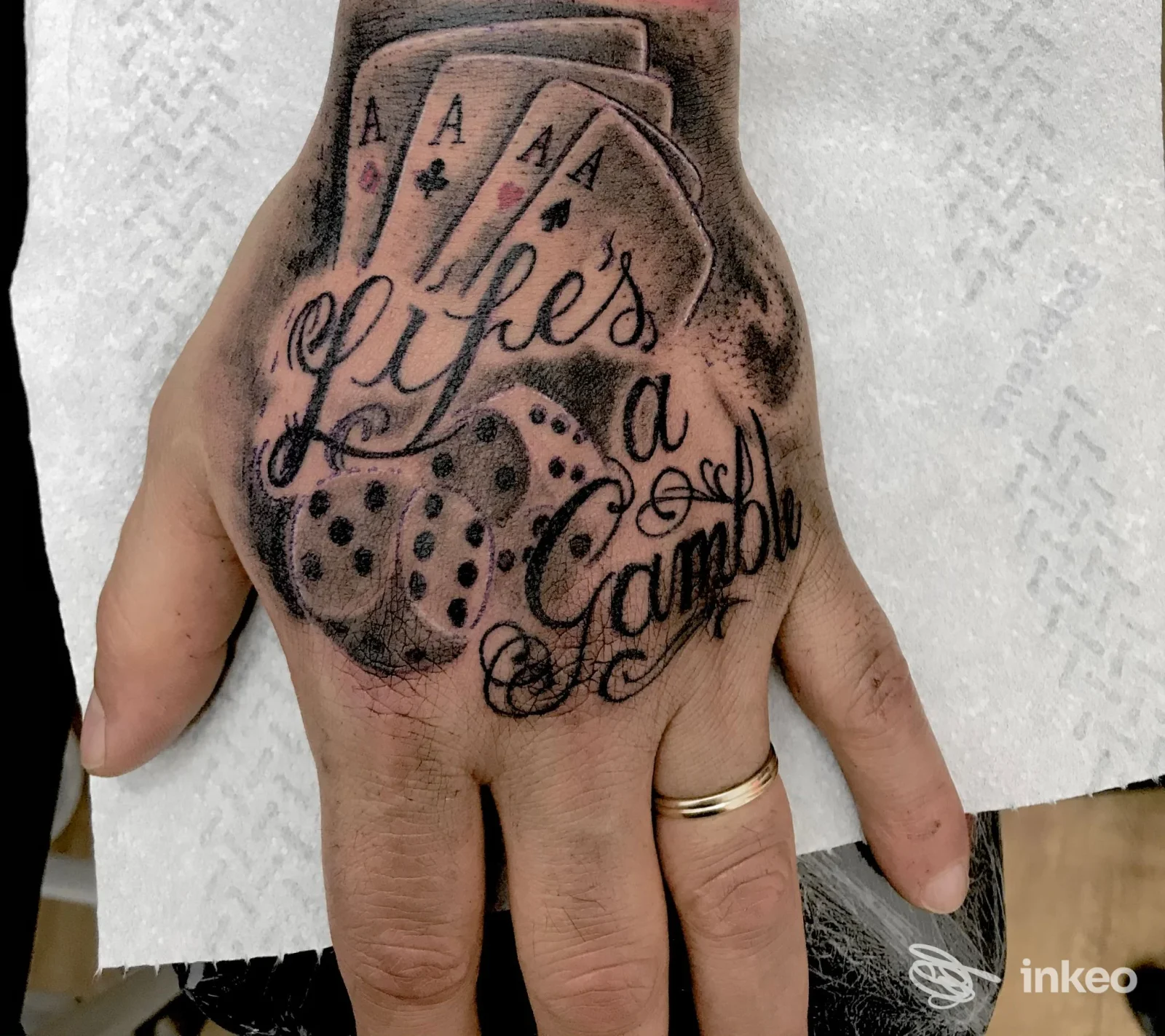 Tatuaggio sul dorso della mano con carte, dadi e scritta “Life's a Gamble”, immagine fornita da TANIA TATTOO, Piediripa.