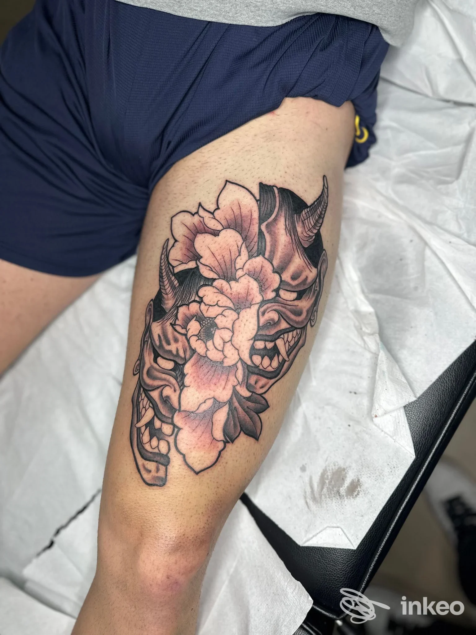 Foto di un tatuaggio sulla coscia che raffigura una maschera oni e fiori, lavoro realizzato da Tattoo moh a Montelabbate in ambiente di studio.