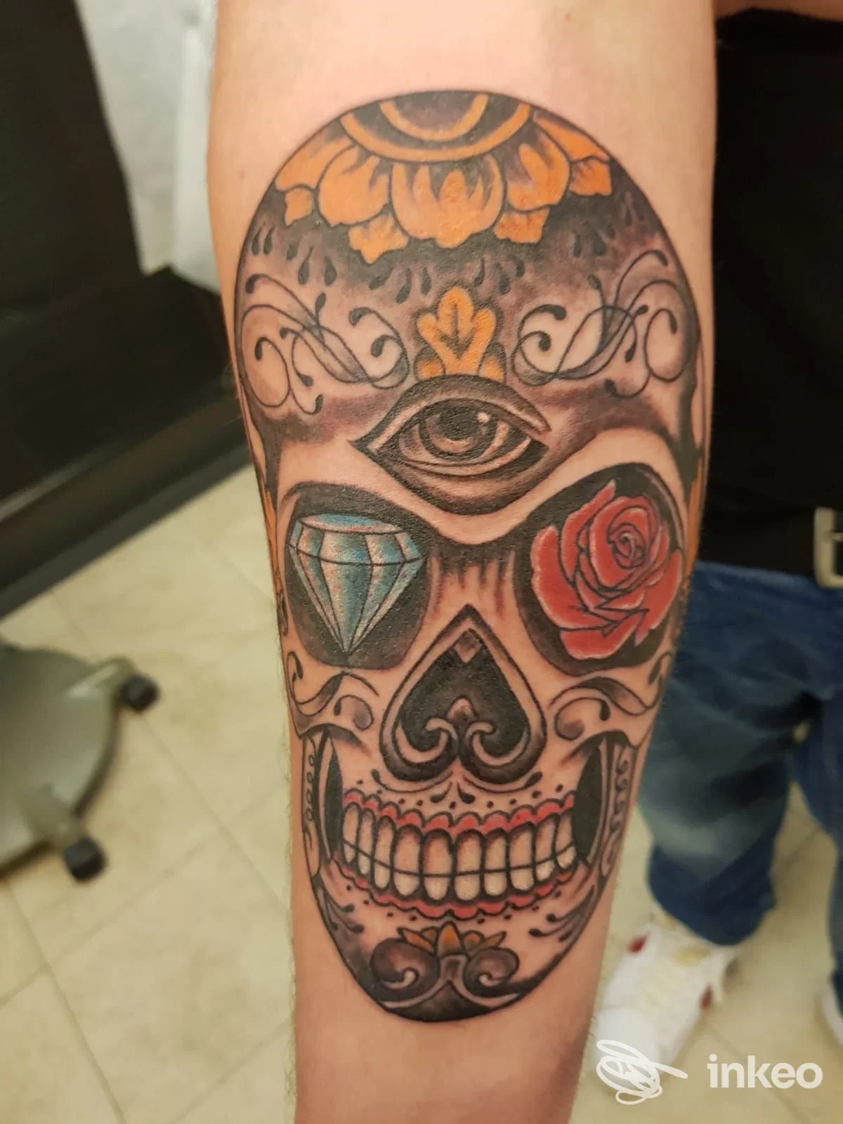 Tattoo sugar skull su avambraccio, con occhio centrale, rosa e diamond, motivi ornamentali e colori vividi.