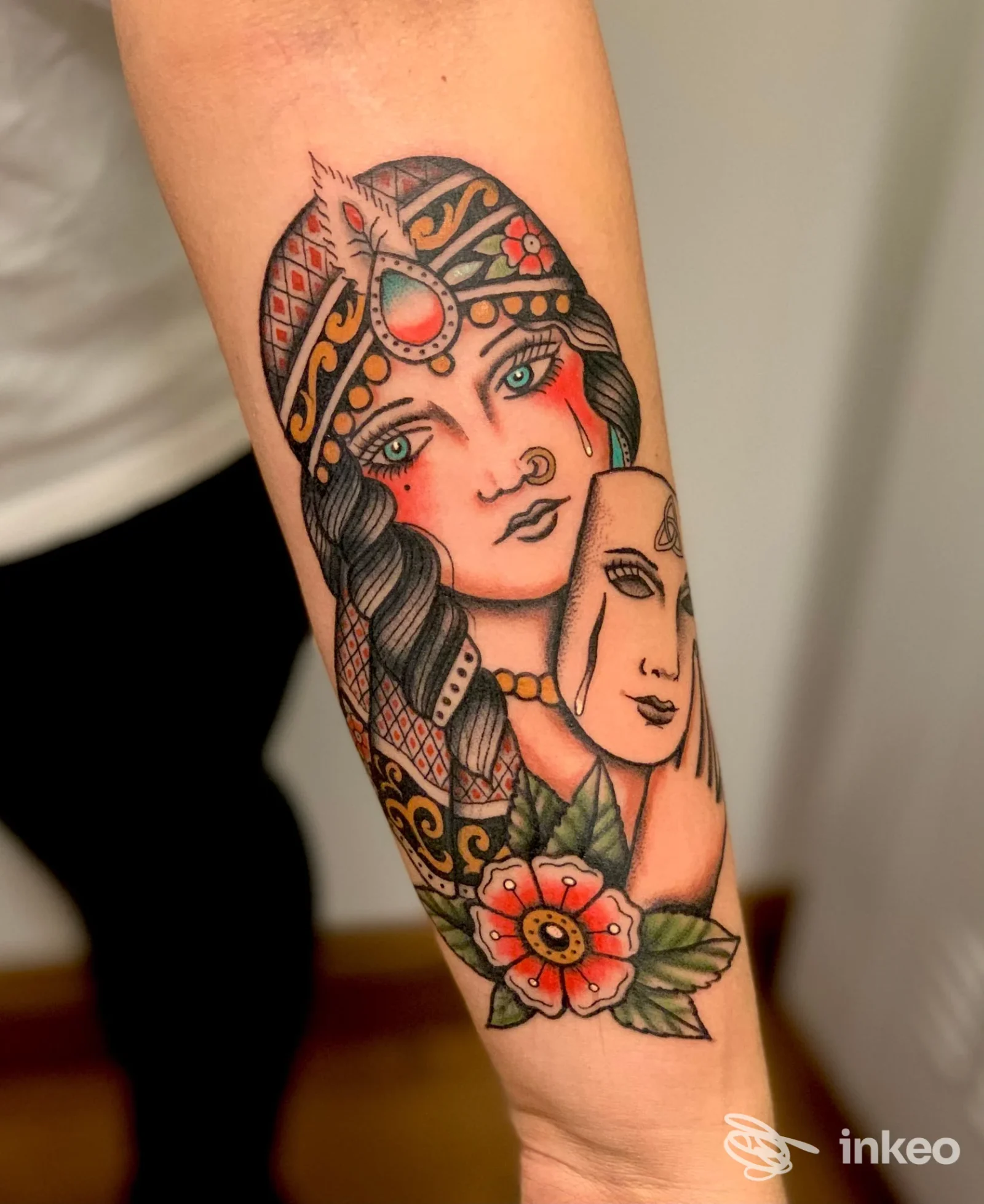 Tatuaggio colorato su avambraccio raffigurante una donna con maschera e fiore, Tattooing Room, Appignano.