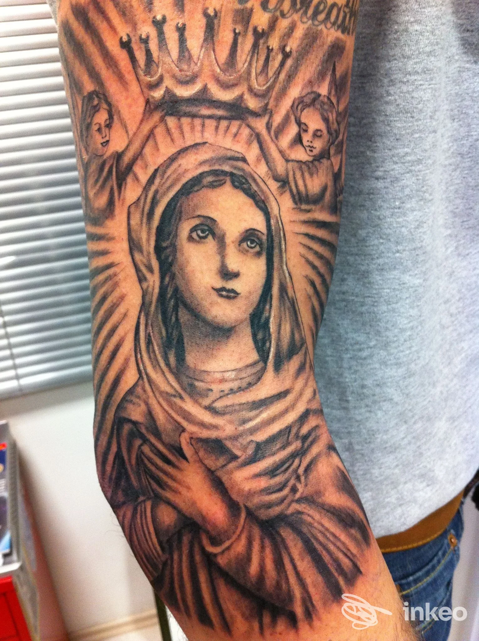 Dettagliato tatuaggio realistico raffigurante la Madonna coronata con angeli sull'avambraccio, realizzato da Tatuaggi SPUNKTATTOO di Enrico Ferracuti a Civitanova Marche.