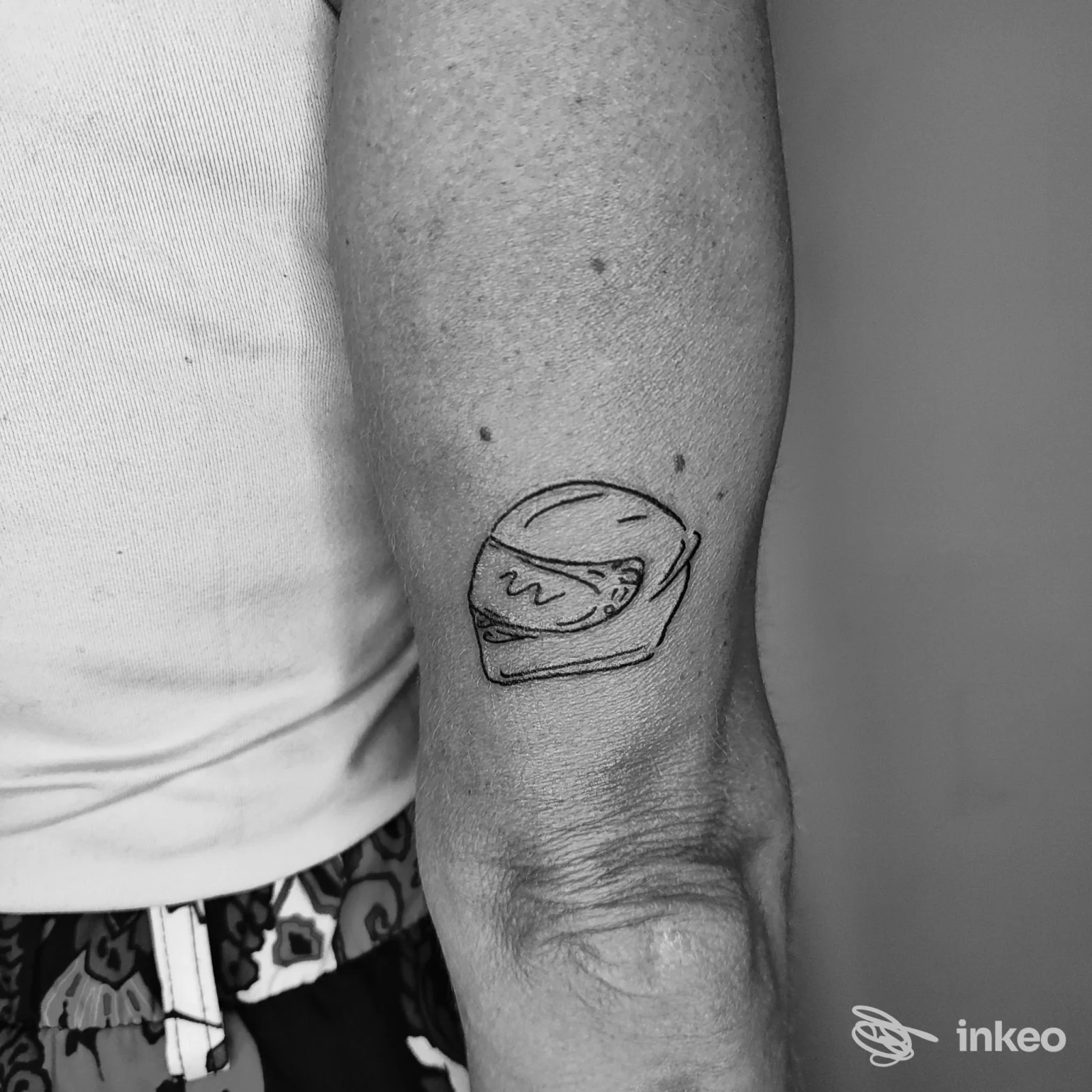 Piccolo tatuaggio a linee nere di un casco sul braccio vicino al gomito, realizzato da Tatuaggi The Monkey studio a Porto San Giorgio.