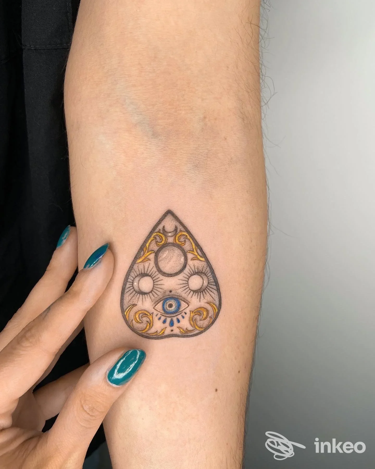 Tatuaggio decorativo su avambraccio con elementi circolari e un occhio blu, foto fornita da Velvet Tattoo Studio, Passo di Treia.