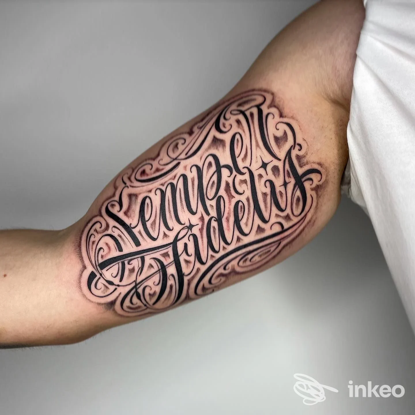 Tatuaggio ornato con testo script sull’avambraccio sinistro, stile elaborato con linee nere e sfumature rosa, visibile senza volto né elementi promozionali.