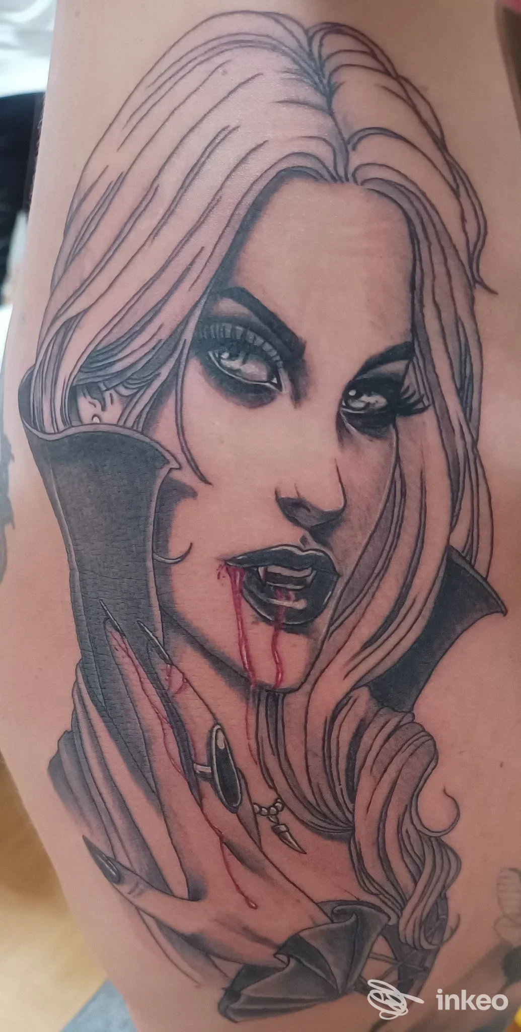 Tatuaggio visibile su avambraccio: ritratto di donna vampira con sangue dalle labbra, linee nette e sfumature, sul braccio sinistro.