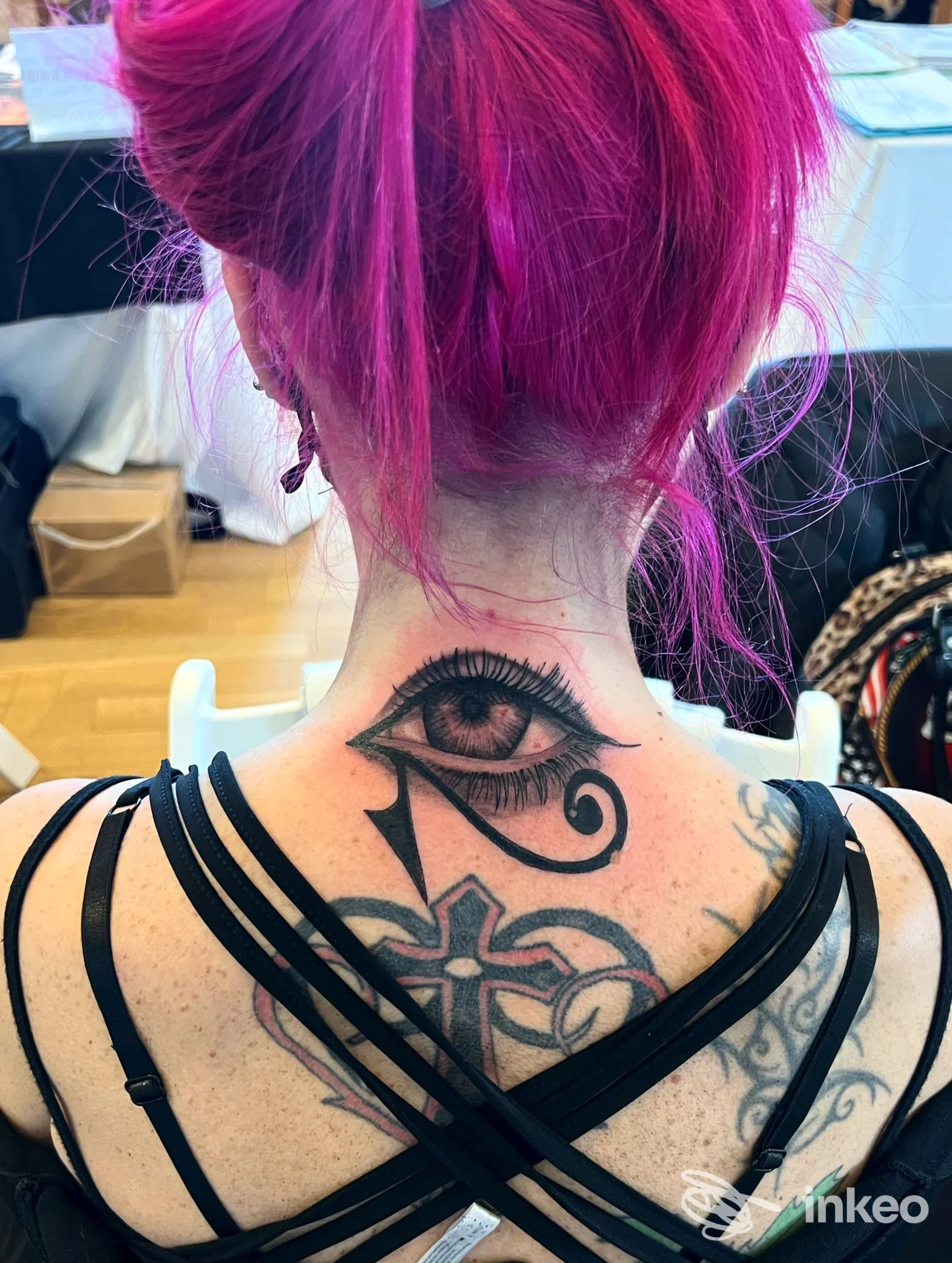 Tatuaggio sulla nuca raffigurante un occhio stilizzato, visibile sulla schiena alta della persona, con capelli rosa acceso.