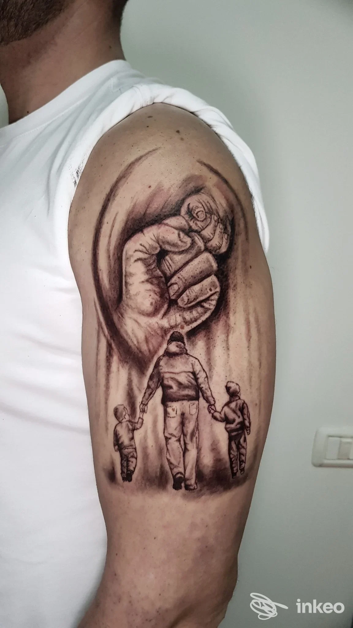 Tatuaggio realistico in bianco e nero sul braccio superiore con un pugno e una figura adulta che tiene per mano due bambini. La Suerte Tattoo Studio, Campobasso.