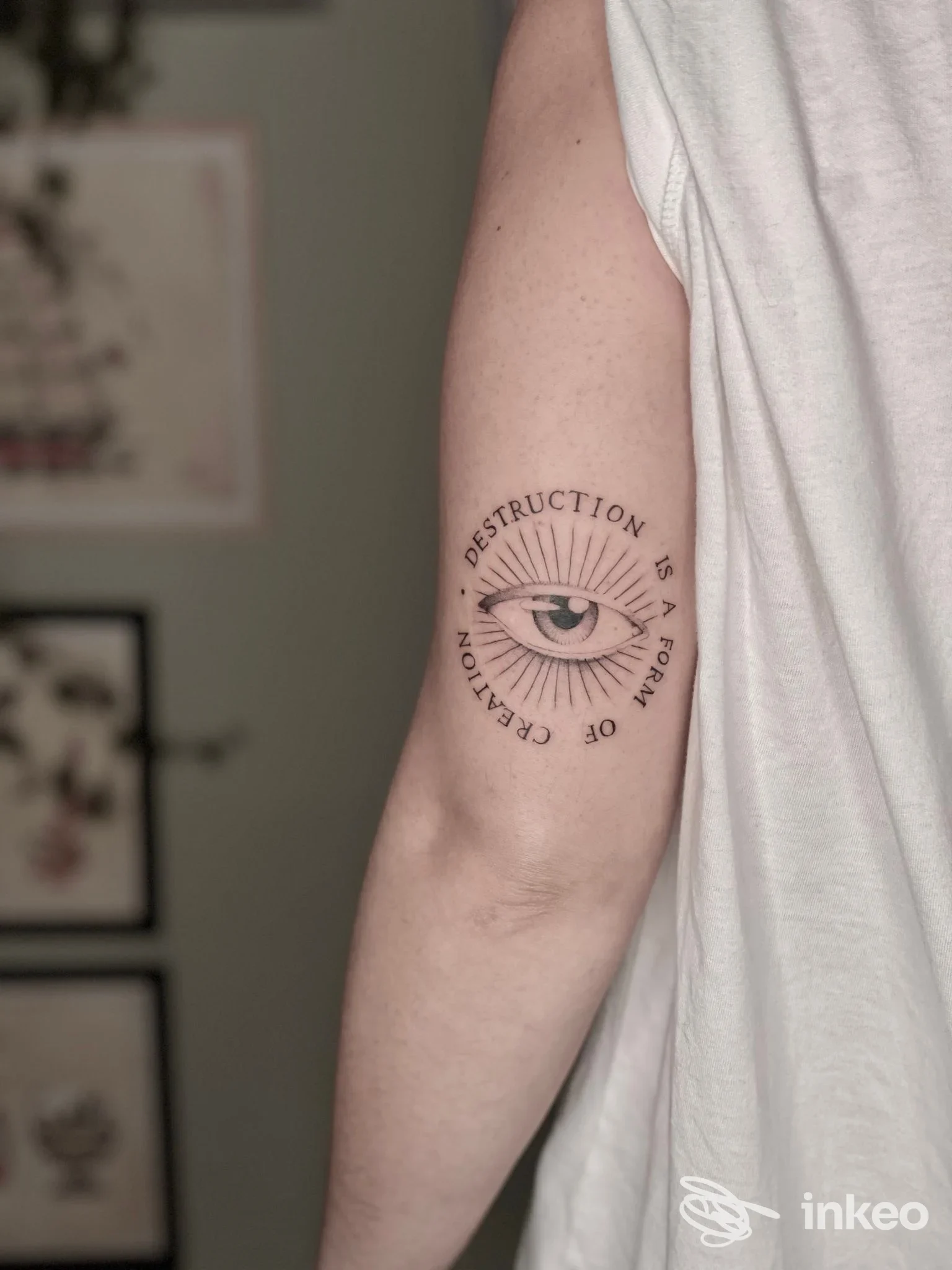 Tatuaggio a inchiostro nero raffigurante un occhio con raggi e testo circolare sul tricipite, foto per Sangue e Lacrime Tattoo, Campomarino.