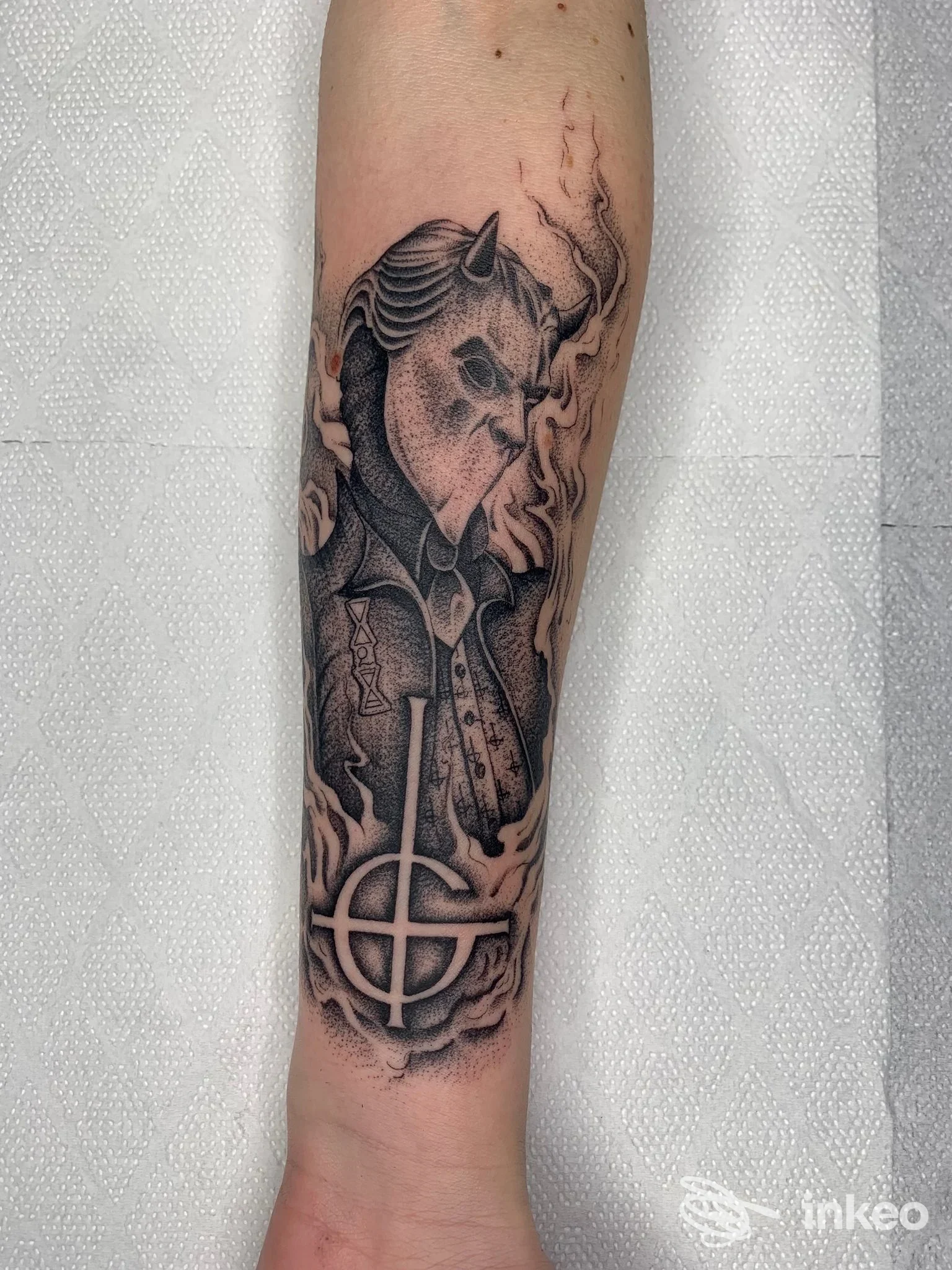 Tatuaggio in bianco e nero su avambraccio: maschera demoniaca con fiamme e simbolo circolare. Black Matter Tattoo Shop, Campobasso.