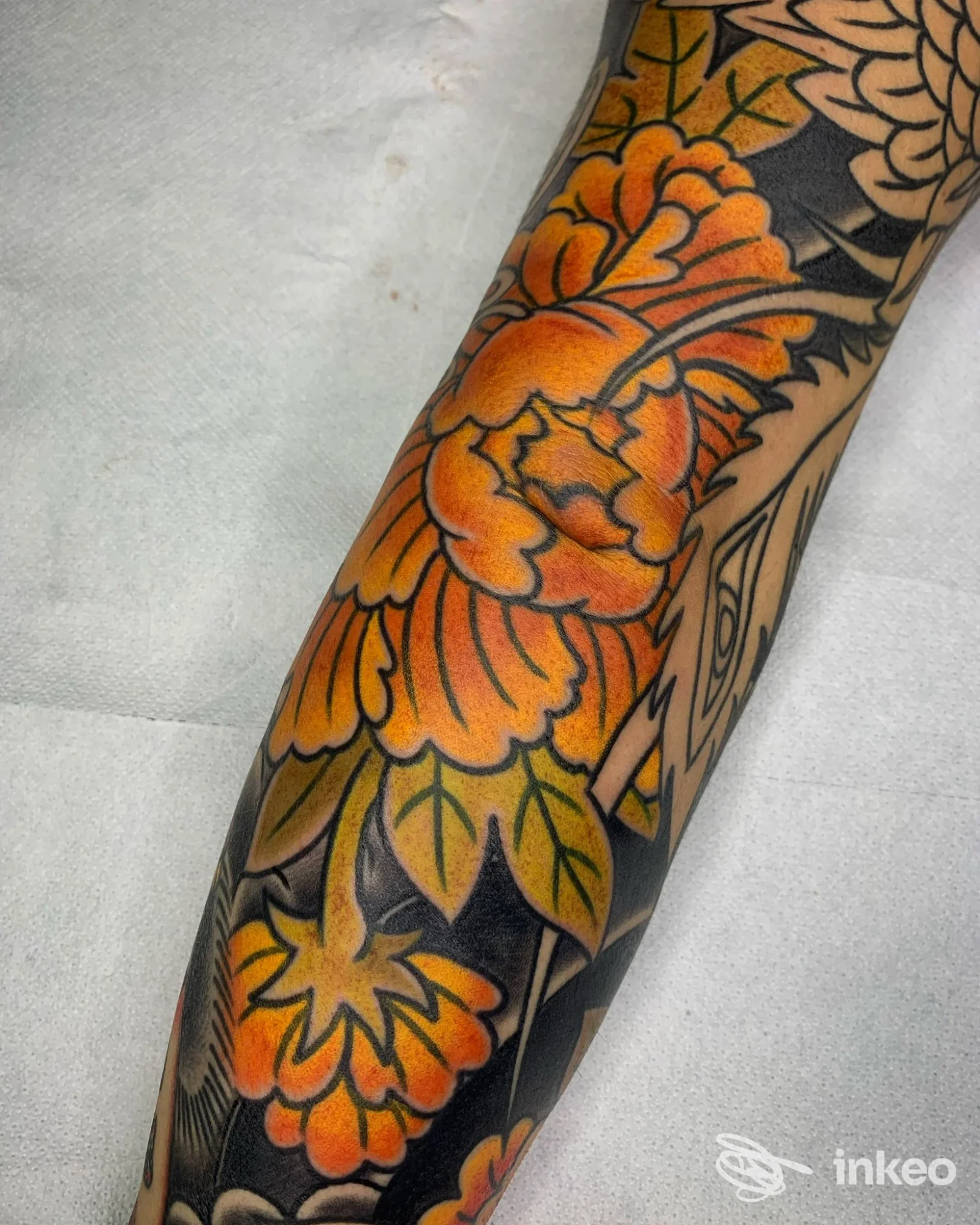 Manica parziale con motivo floreale arancione e foglie verdi su avambraccio, foto dello studio Black Matter Tattoo Shop, Campobasso.