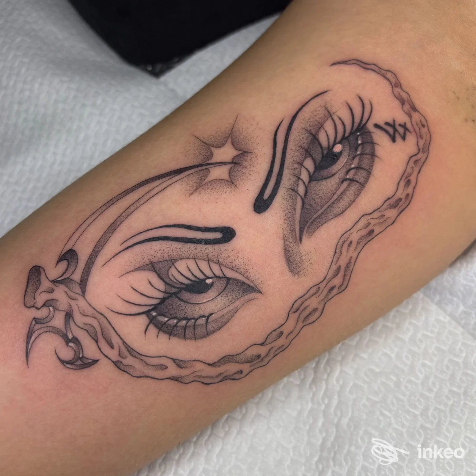 Tatuaggio in bianco e nero con due occhi stilizzati sull'avambraccio, foto di Fine Line Cutting tattoo shop a Campobasso.