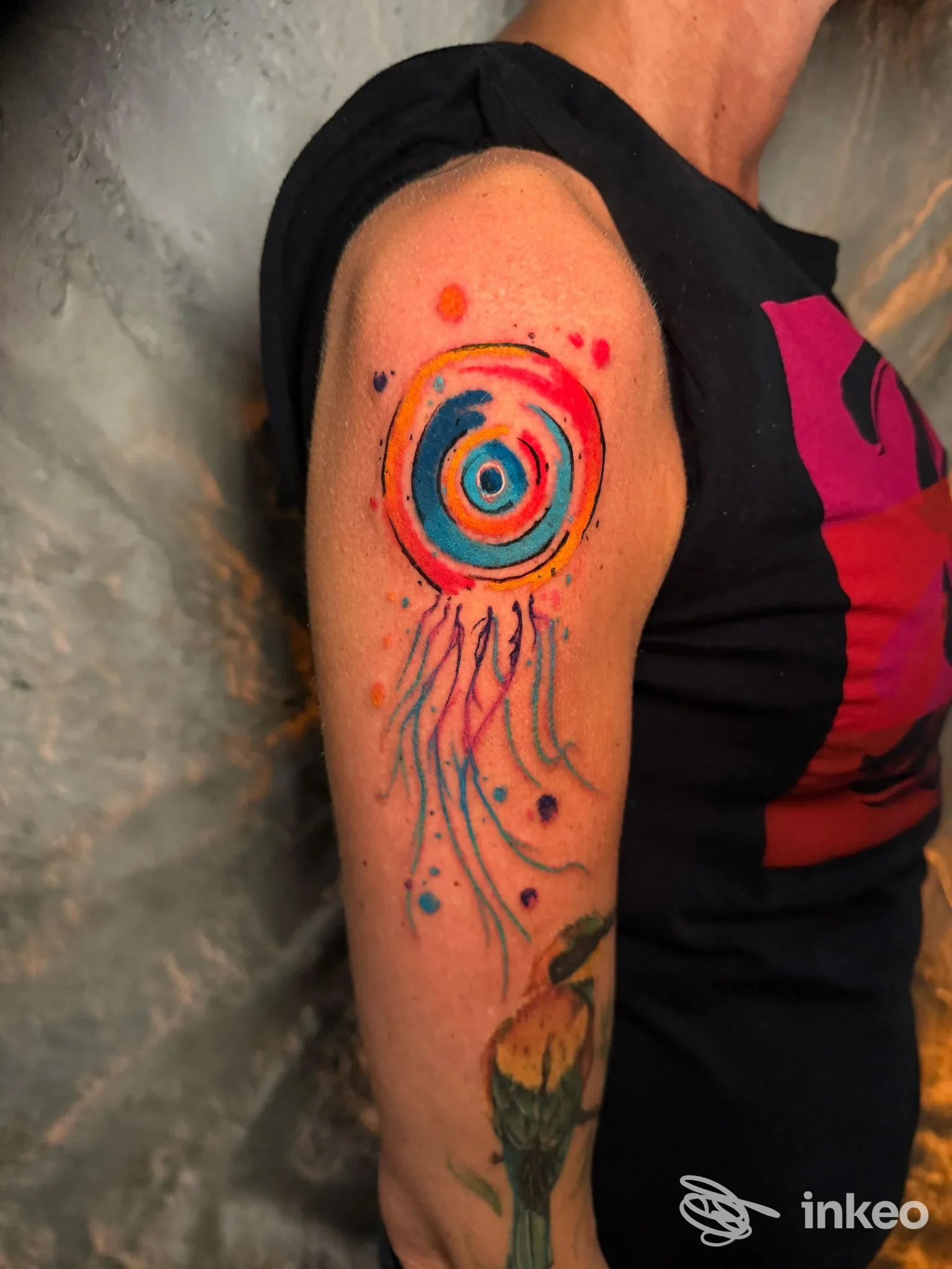 Tatuaggio watercolour sul braccio superiore con cerchio concentric o e code fluide, foto fornita da 24 Tattoo Studio, Carmagnola.