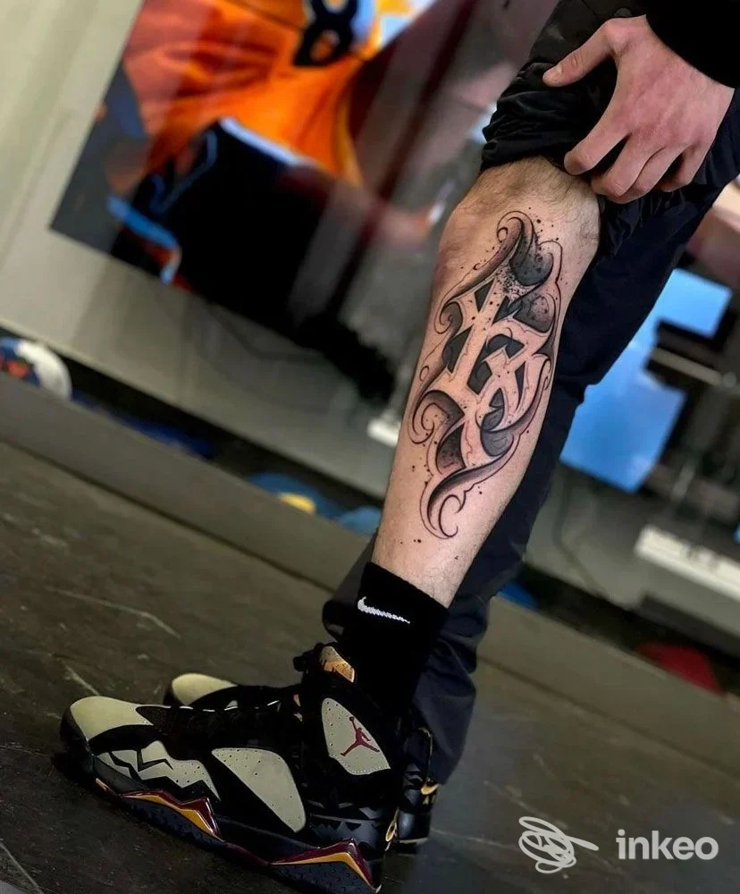 Primo piano di tatuaggio lettering ornamentale sul polpaccio, 24 Tattoo Studio Carmagnola, Carmagnola.