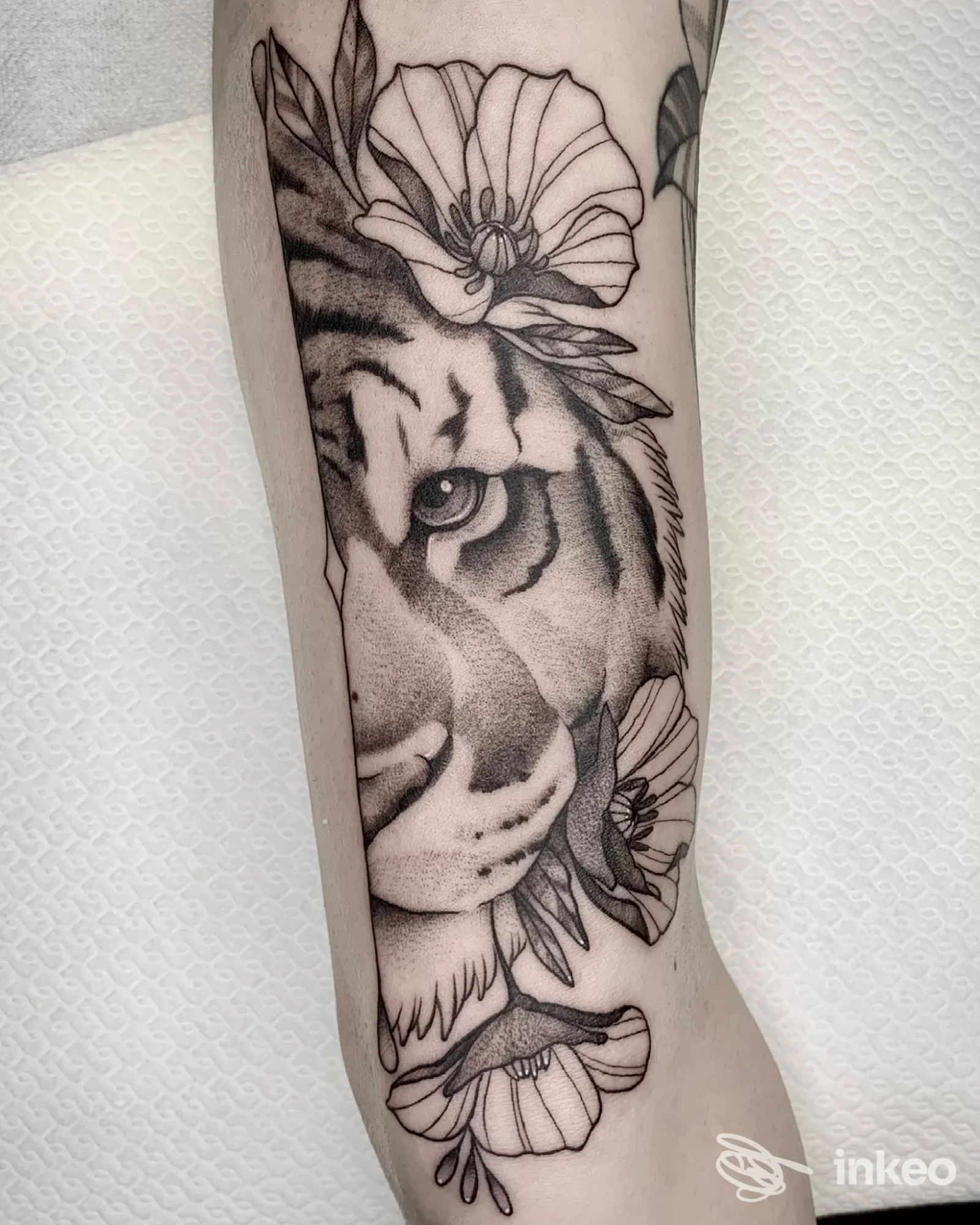Tatuaggio in bianco e nero di mezza testa di tigre e fiori sull'avambraccio, fotografia inviata per Aline Blanc Tattoo Shop, Torino.
