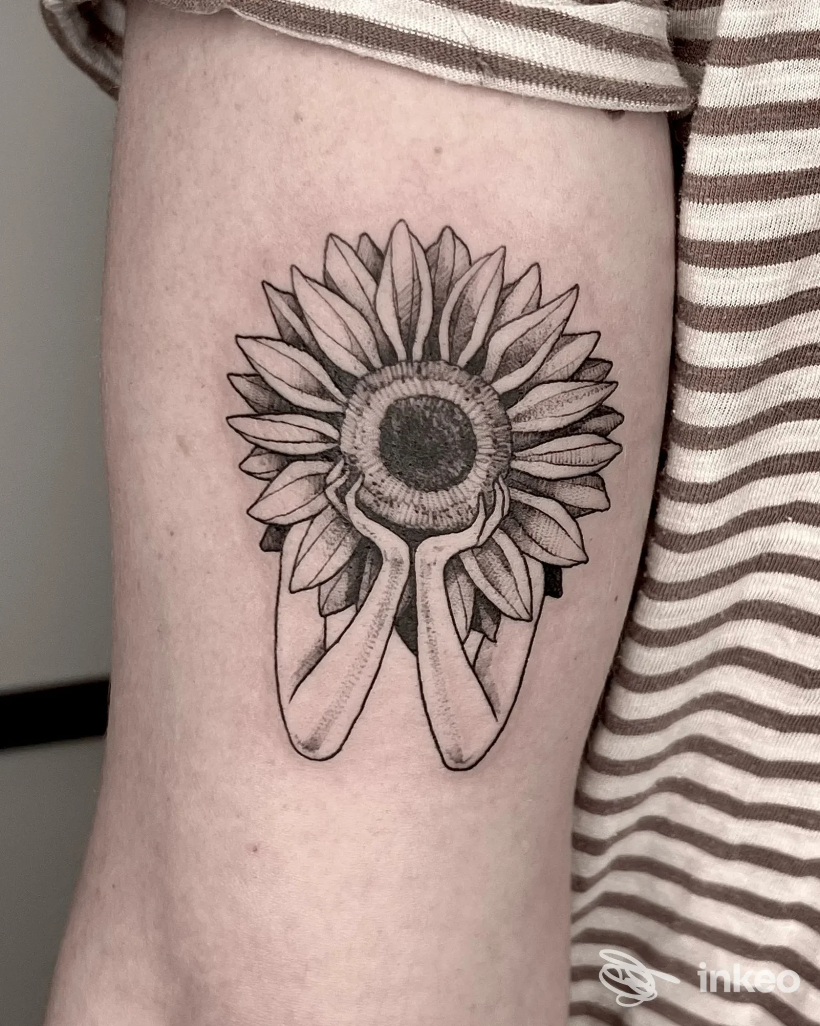 Tatuaggio girasole stilizzato con mani sulla parte superiore del braccio, foto da Aline Blanc Tattoo Shop, Torino.