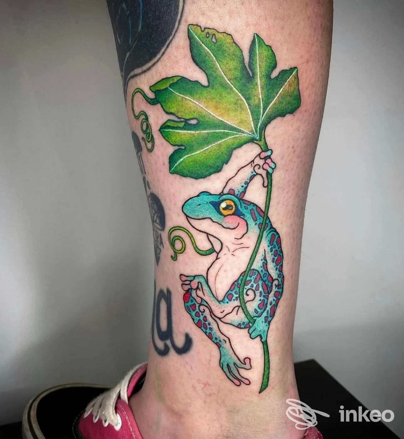 Tatuaggio colorato di rana appesa a una foglia sulla parte inferiore della gamba, foto fornita da Alma Libre Tattoo Studio, Casale Monferrato.