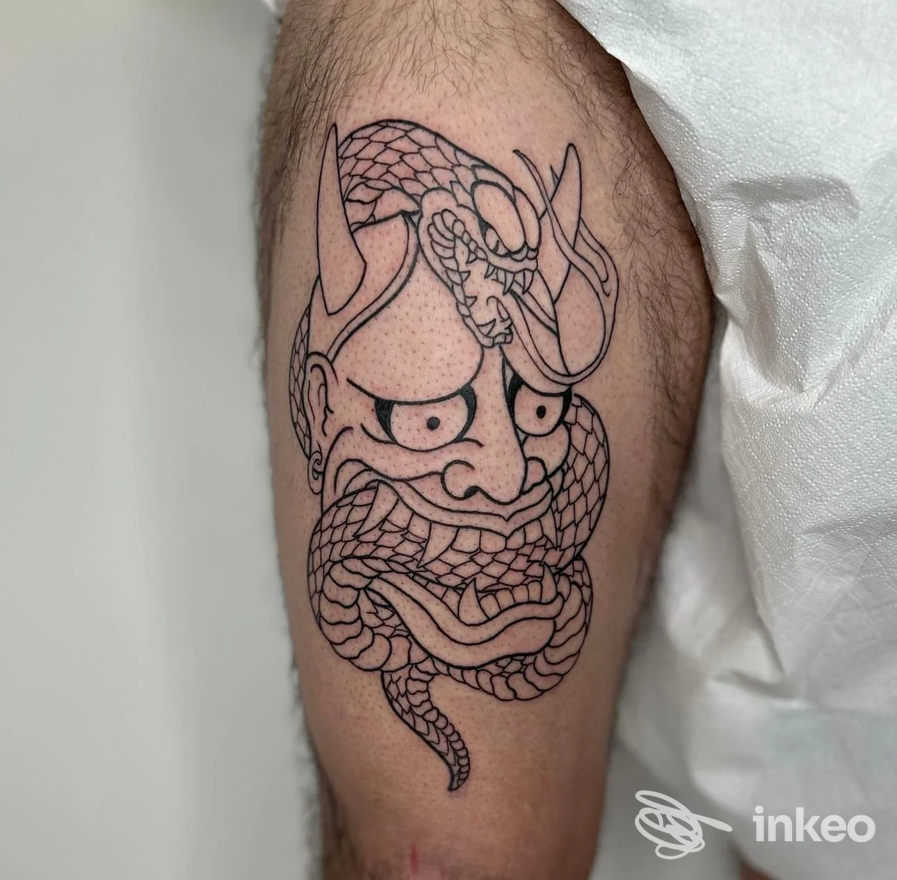 Tatuaggio linework su coscia: maschera stilizzata avvolta da un serpente. Alma Libre Tattoo Studio, Casale Monferrato.