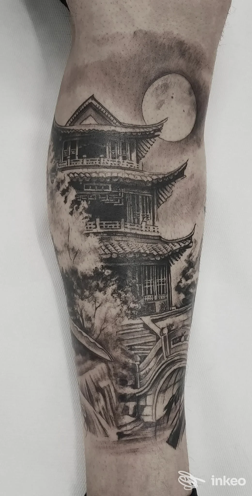 Tatuaggio black & grey su polpaccio raffigurante edificio a più piani e luna — Ainos Tattoo, Torino.