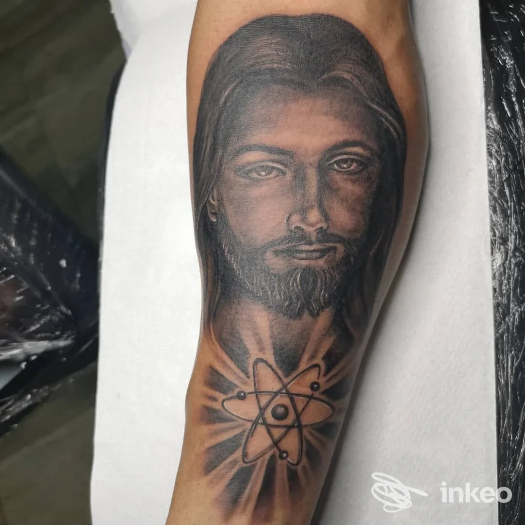 Tatuaggio realistico in bianco e nero su avambraccio: ritratto maschile con simbolo atomico. Alpignano Ink, Alpignano.