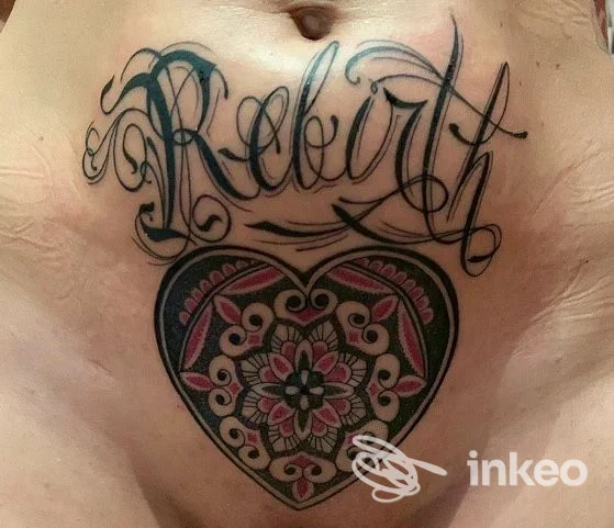 Tatuaggi sul basso addome: scritta calligrafica 'Rebirth' e cuore ornamentale colorato. Ars Tattoo, Moncalieri.