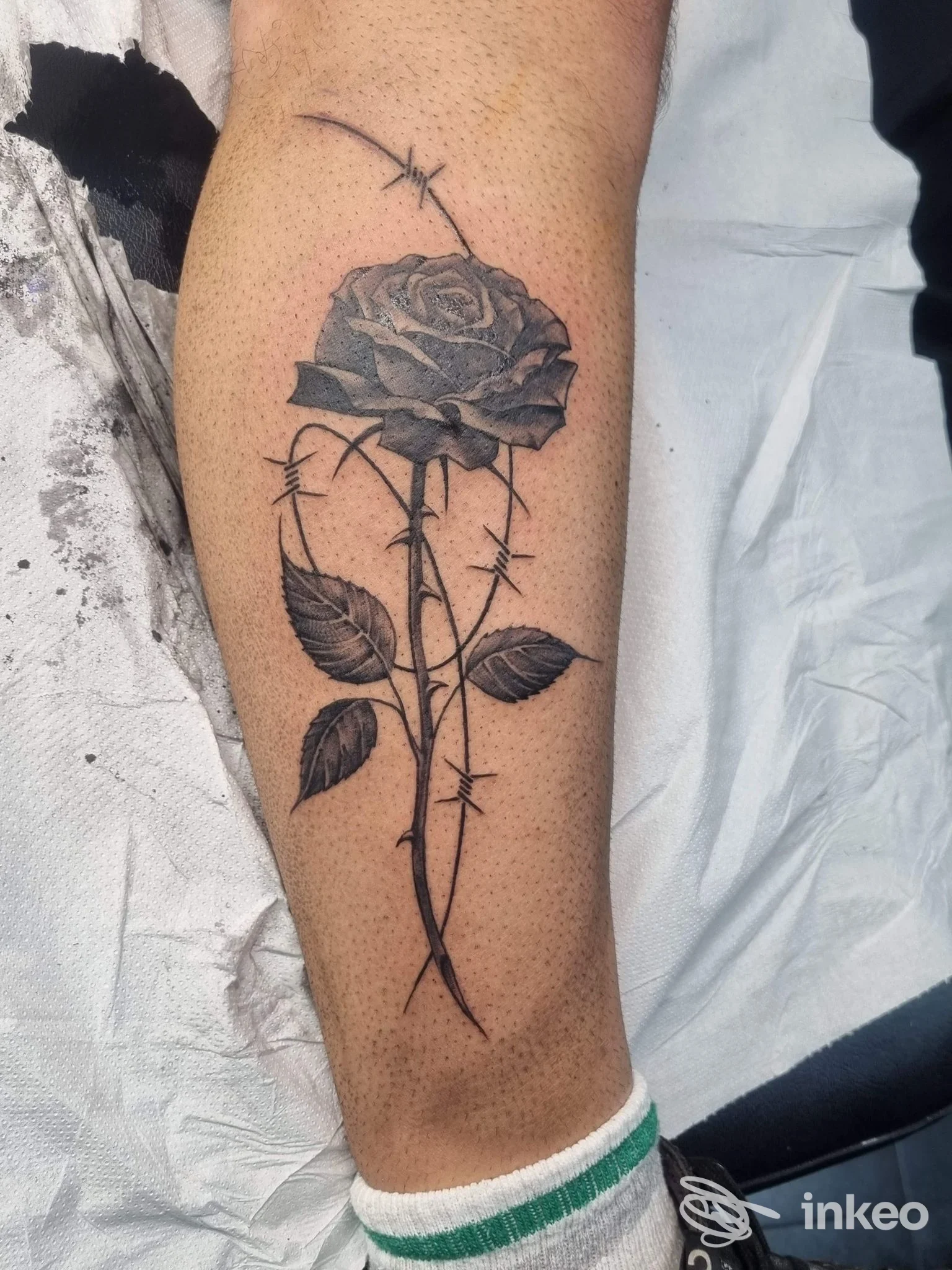 Tatuaggio di una rosa avvolta da filo spinato sul polpaccio, eseguito da Black Art Tattoo a Torino, nero-grigio con ombreggiature dettagliate.