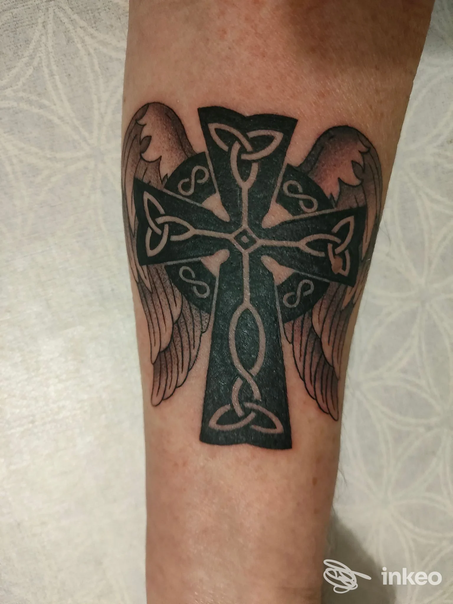 Tatuaggio a inchiostro nero: croce celtica con intrecci e ali sull'avambraccio, dettaglio fotografico. Buum Tattoo Studio - Torino, Moncalieri.