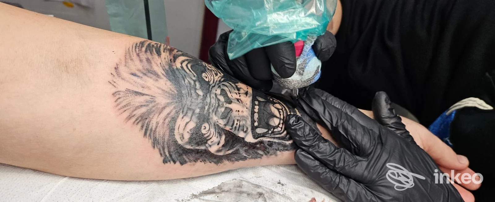 Tatuaggio in nero e grigio in corso sull'avambraccio, artista con guanti neri al lavoro nello studio Cani Sciolti Tattoo&Piercing a Torino.