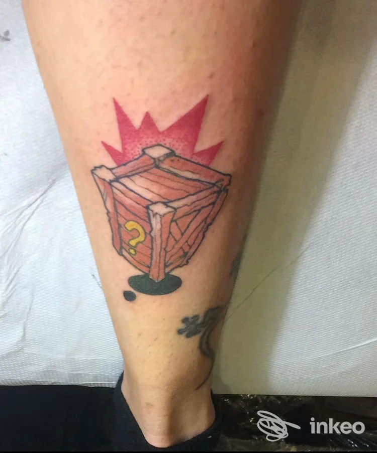 Tatuaggio su polpaccio raffigurante una cassa di legno con punto interrogativo, immagine inviata da Cani Sciolti Tattoo&Piercing a Torino.