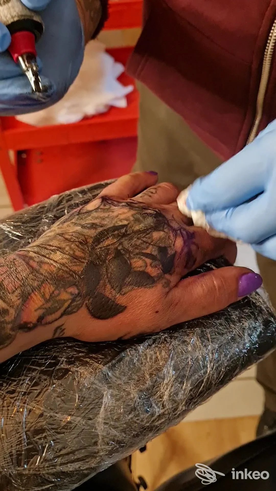 Primo piano della mano tatuata mentre viene eseguito il lavoro allo studio Compagnia degli Inchiostri a Torino, operatore con guanti e macchinetta.