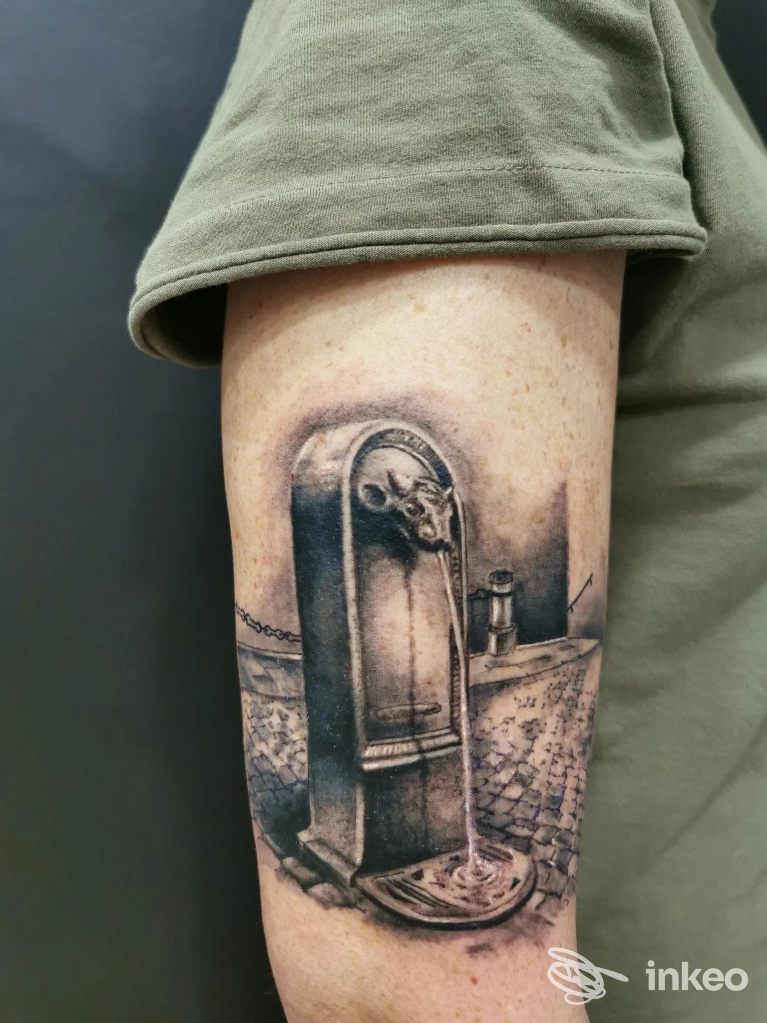 Tatuaggio in bianco e nero di una fontanella su pavé, applicato sul braccio; foto fornita da Diem Tattoo, Torino.