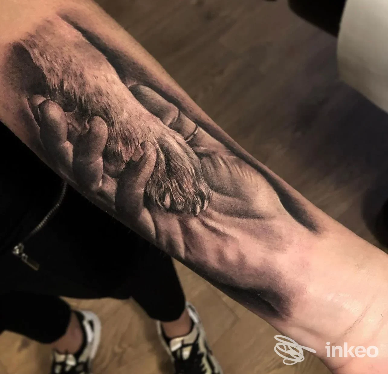 Tatuaggio realistico sull'avambraccio raffigurante una mano che tiene la zampa di un cane, realizzato da Dope Tattoo a Bra.