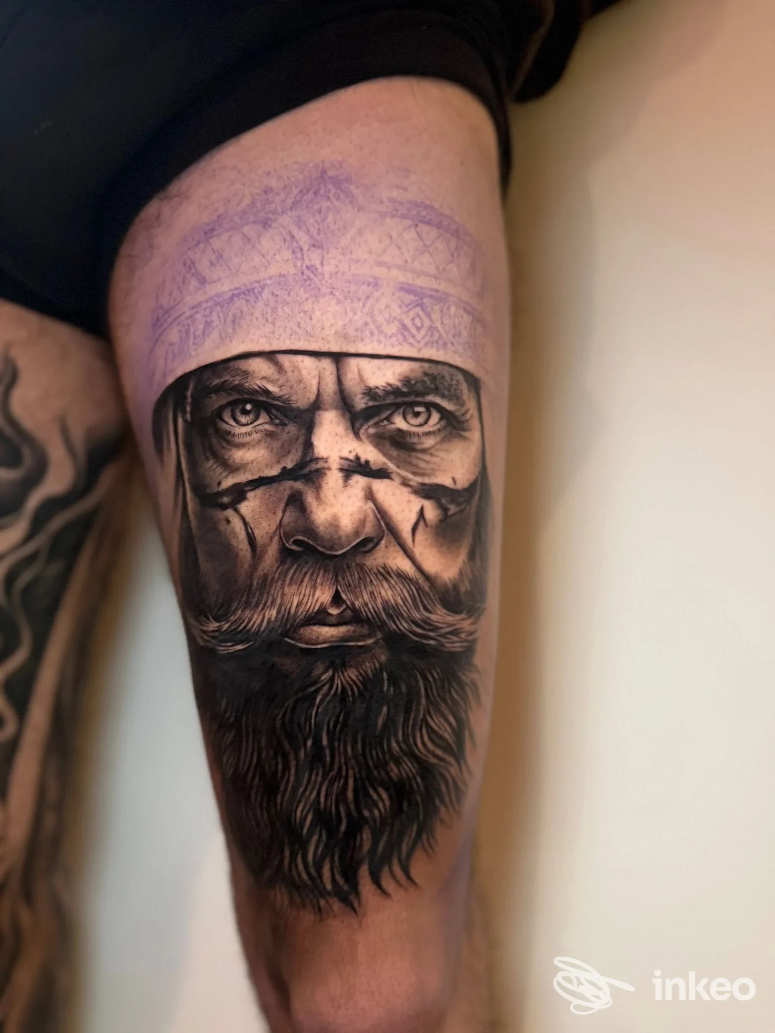 Tatuaggio realistico black-and-grey di un volto barbuto sulla coscia, stencil viola visibile; Fuori Luogo Tattoo, Alpignano.