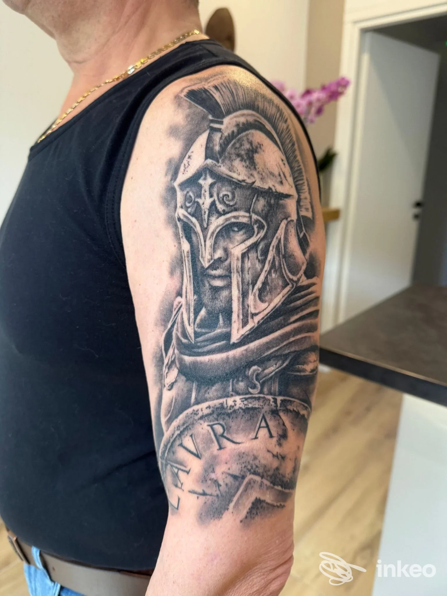 Tatuaggio black & grey di un guerriero con elmo sul braccio superiore, fotografia fornita da Fuori Luogo Tattoo Pmu Trucco Semipermanente Piercing, Alpignano.