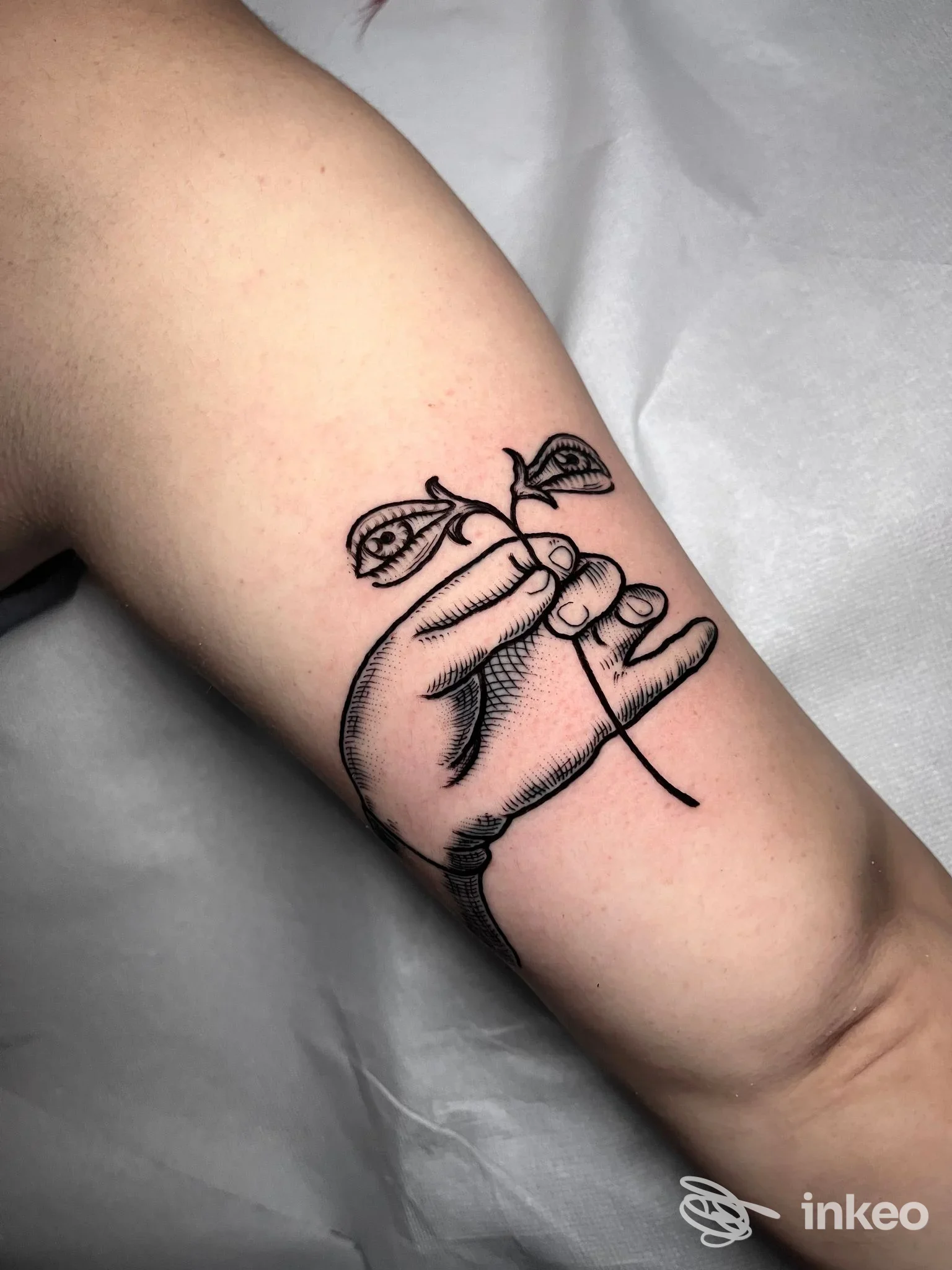 Tatuaggio su braccio raffigurante una mano che tiene un germoglio con due foglie, realizzato in stile linework in bianco e nero.