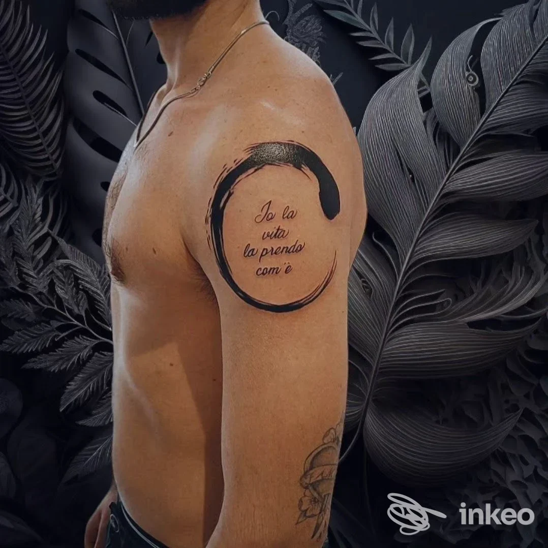 Tatuaggio a cerchio con pennellata nera e scritta ornamentale sull'omero; immagine fornita da Horus tattoo e piercing di Riccardo Ragusano, Borgone Susa.