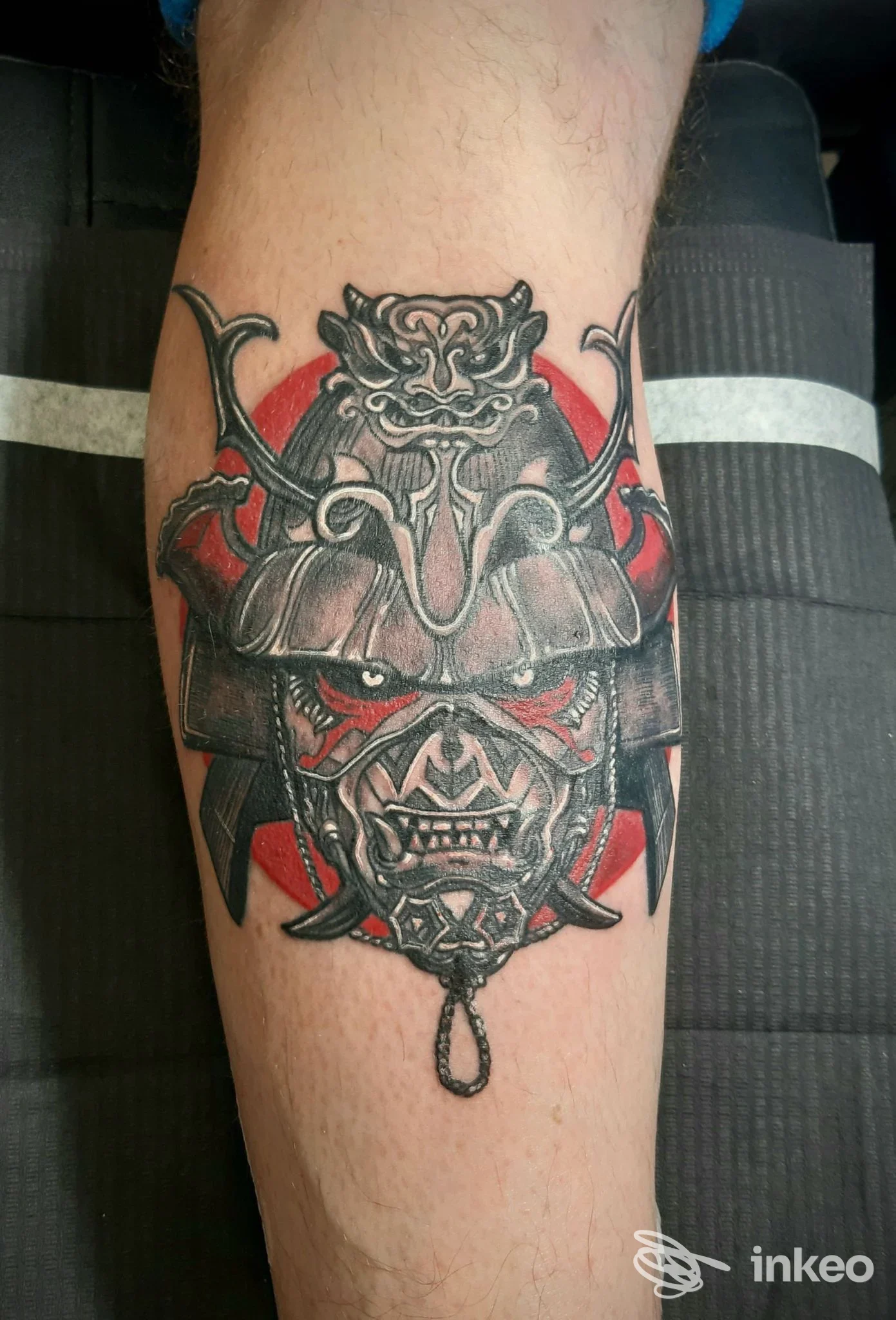 Tatuaggio a tema elmo/maschera samurai nero, grigio e rosso sul polpaccio, fotografato per Greg Tattoo Art Studio a Omegna.