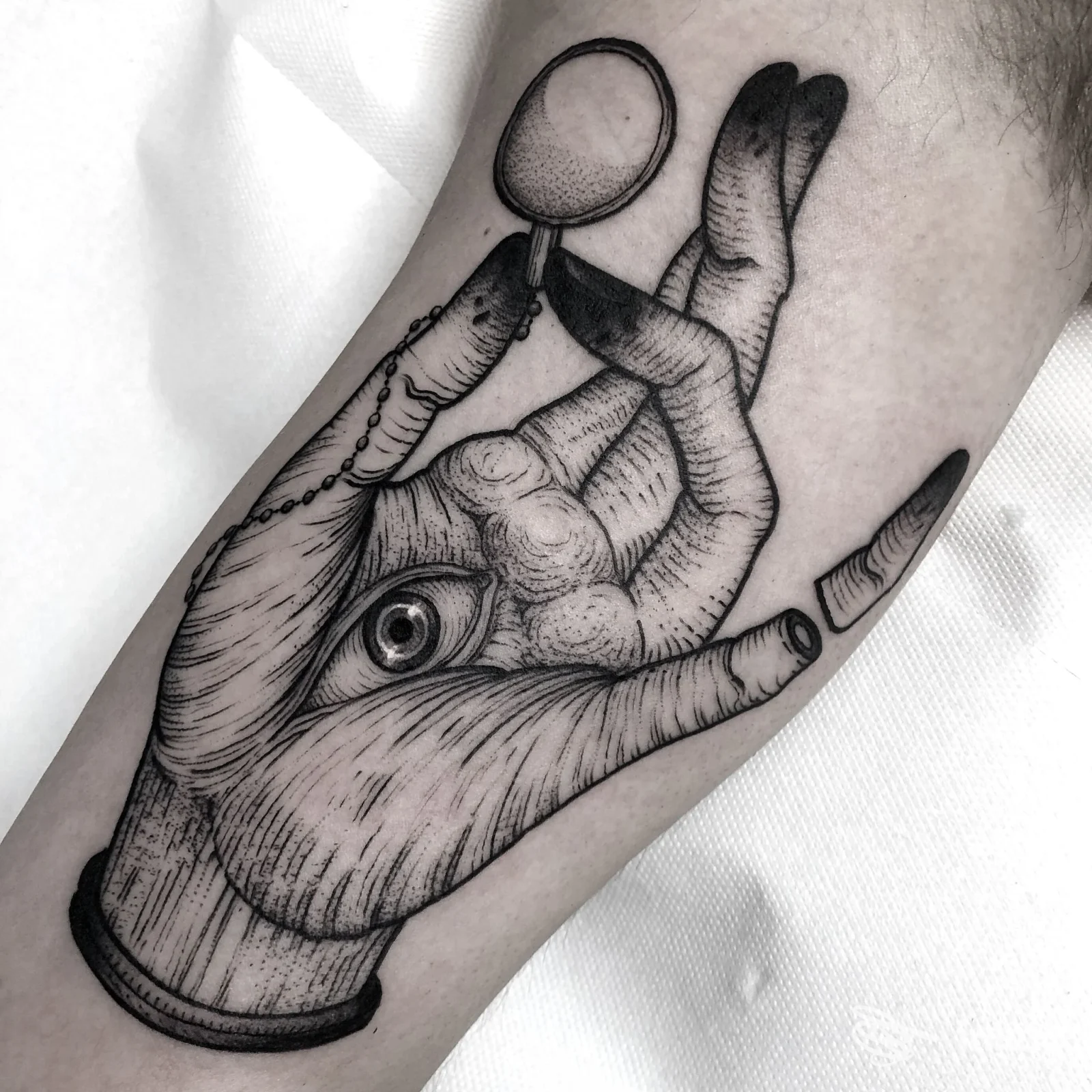 Tatuaggio in bianco e nero su avambraccio raffigurante una mano con un occhio e specchietto, foto fornita da Hardtimes Tattoo, Torino.