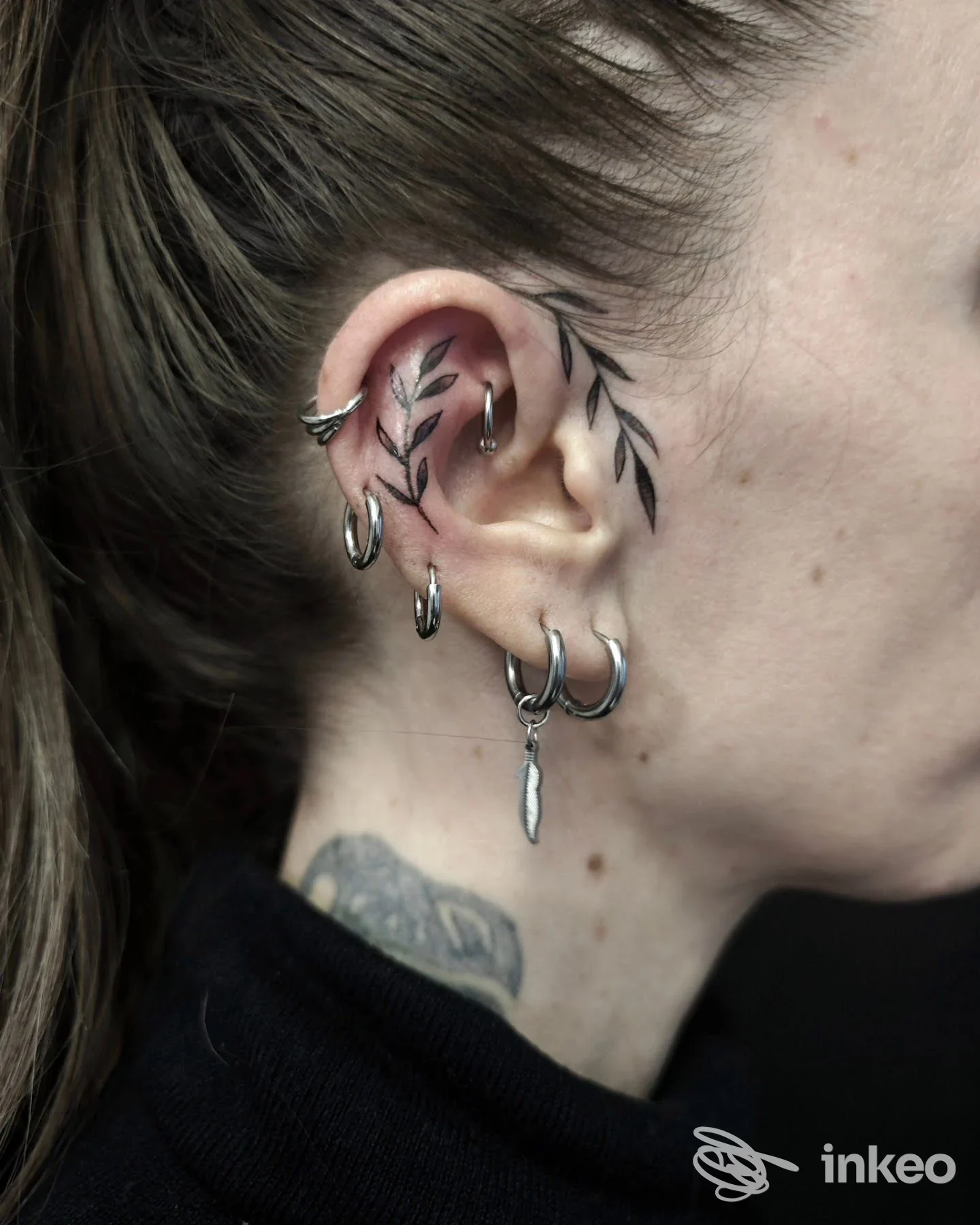 Dettaglio di orecchio con piercing e tatuaggio a foglie in nero, foto fornita da Inkside Stories tattoo studio, Moncalieri.