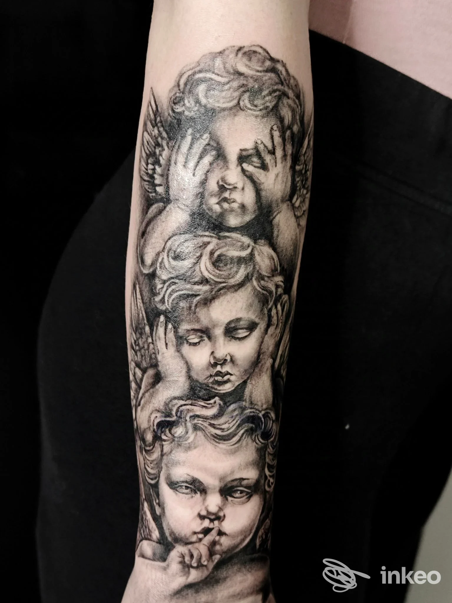 Tatuaggio realistico in bianco e nero su avambraccio con tre cherubini, foto fornita da Inkside Stories tattoo studio, Moncalieri.